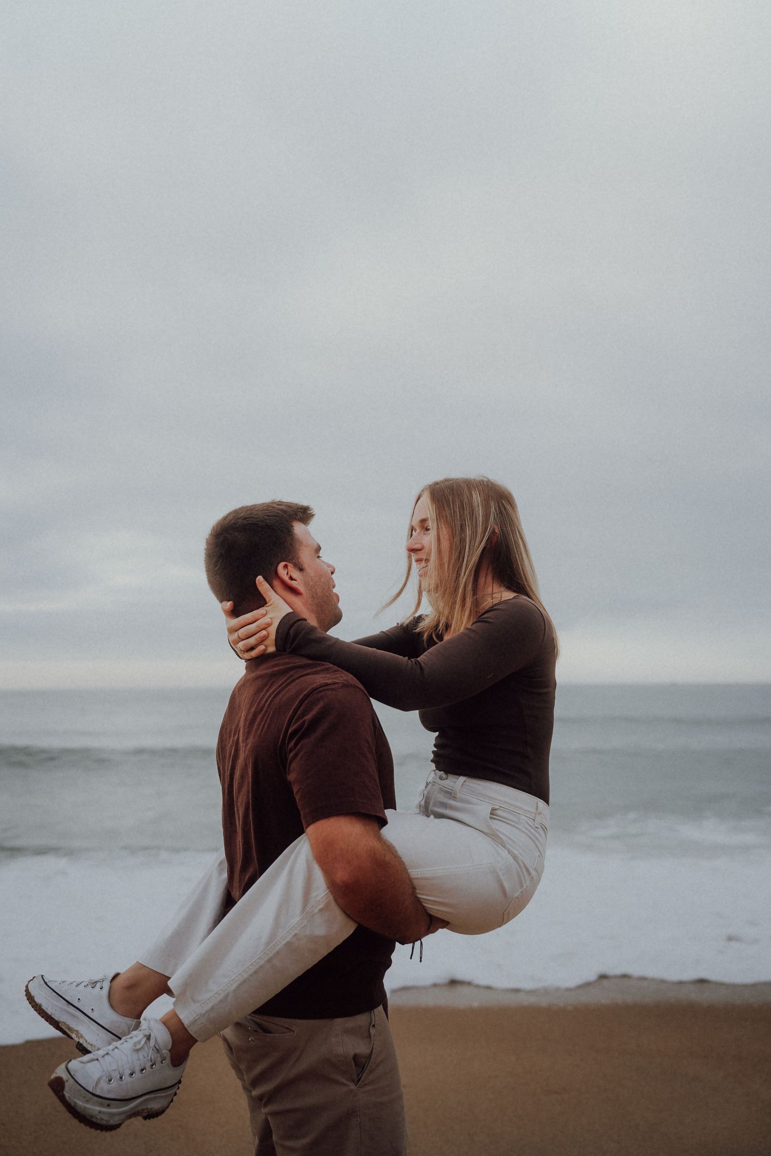 Man lifting woman in his arms on a cloudy beach.