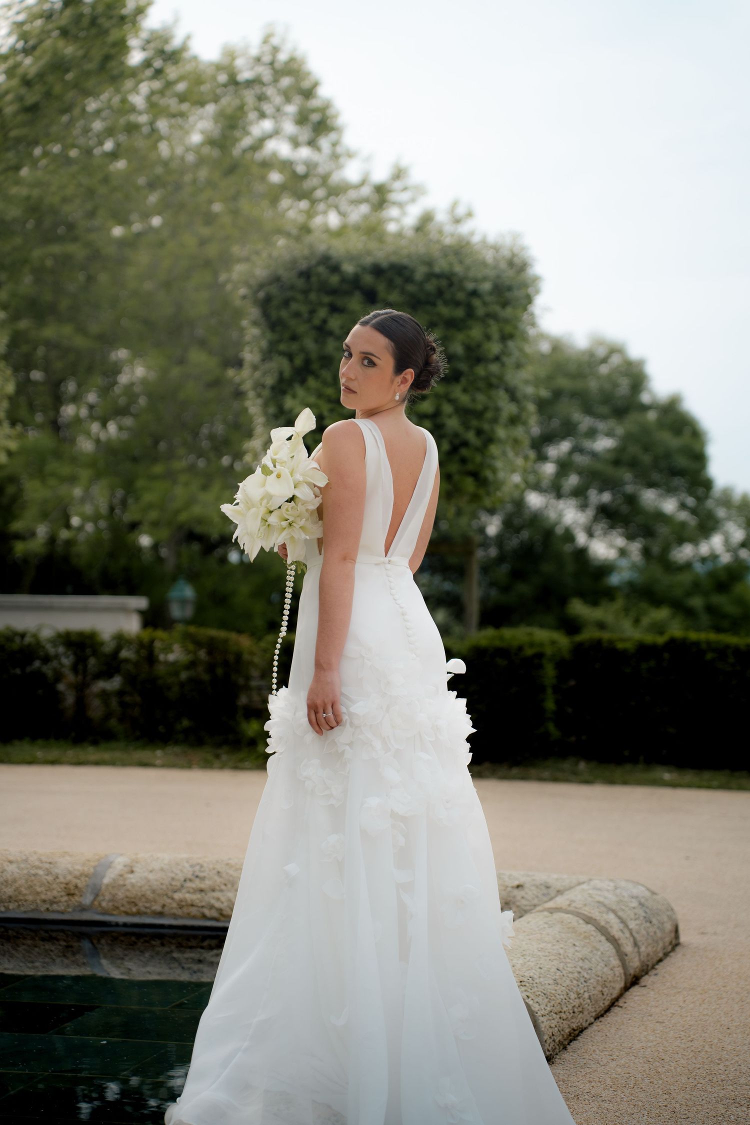 Bride in elegant white gown with deep V-back holding white orchid bouquet.