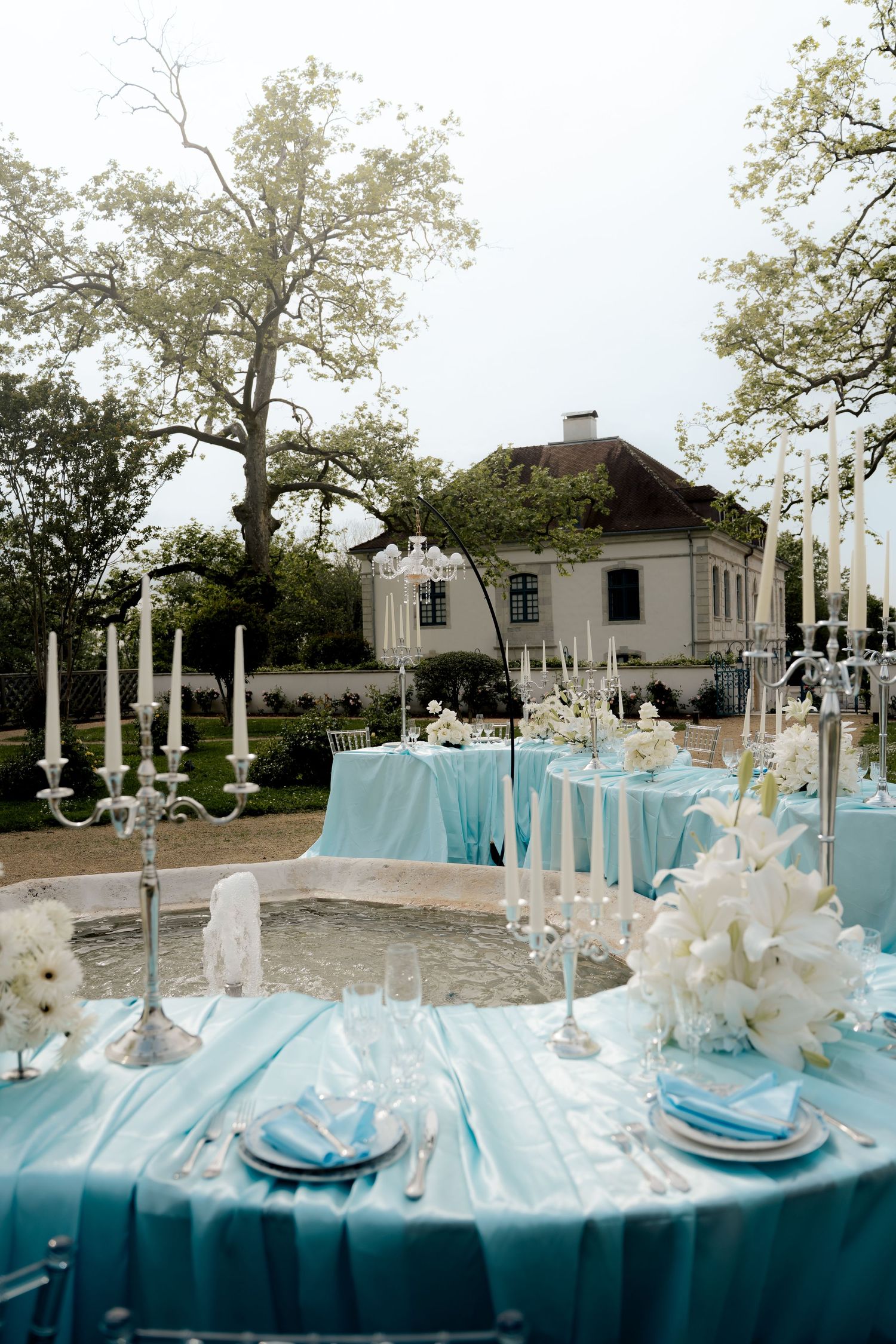 Elegant outdoor wedding reception with blue tablecloths, candelabras, and white flowers near estate.