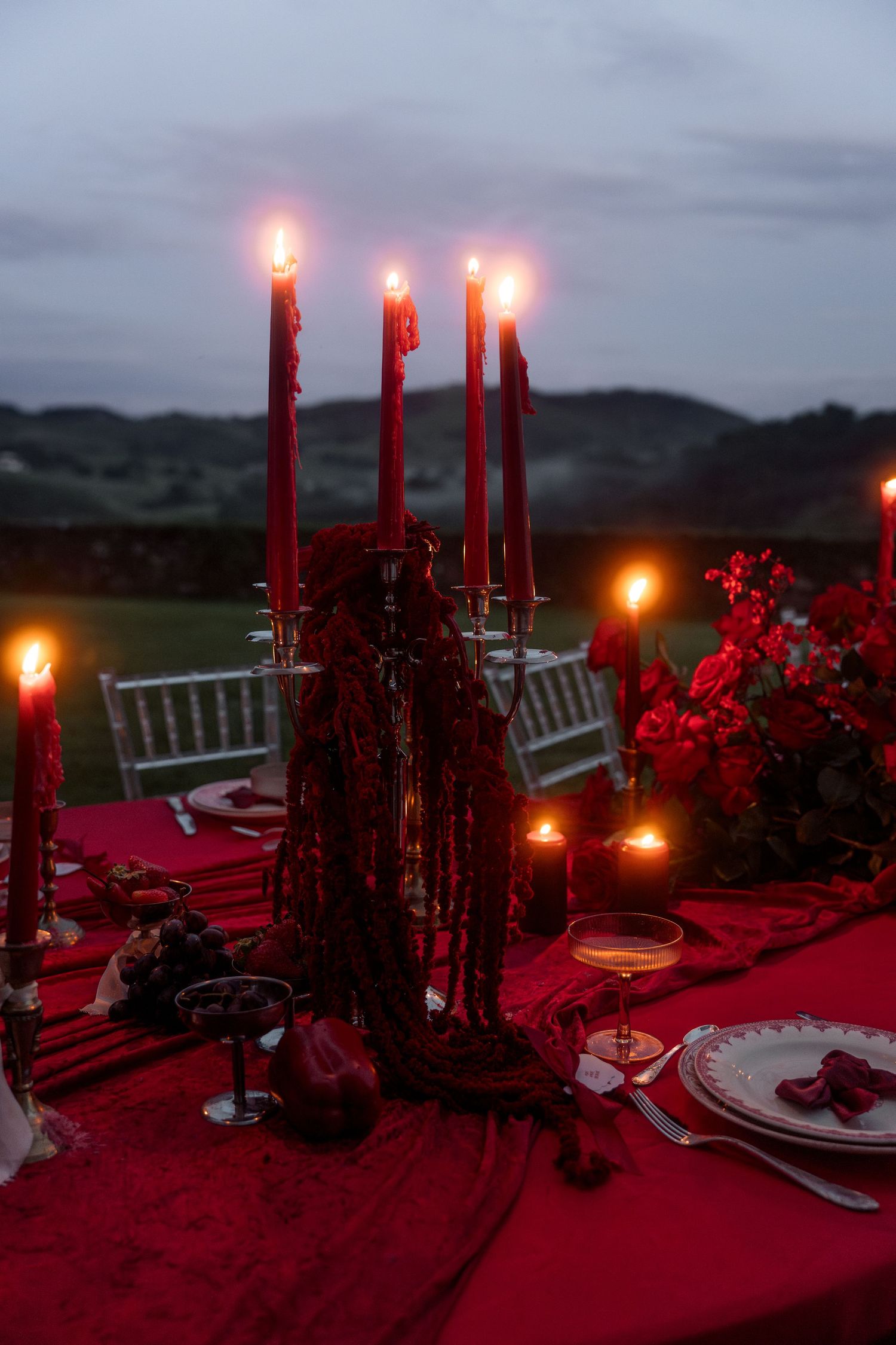 Elegant red candlelit wedding tablescape with tall tapered candles and floral arrangements at dusk.