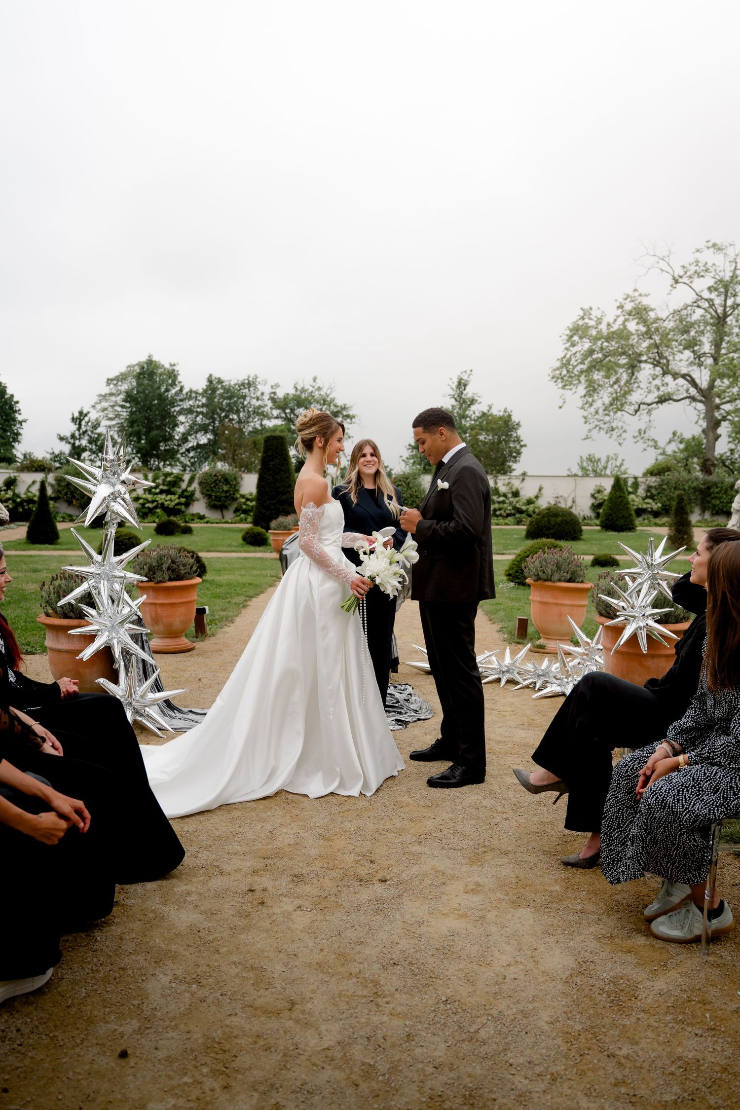 Bride and groom exchanging vows at outdoor garden wedding ceremony with seated guests.