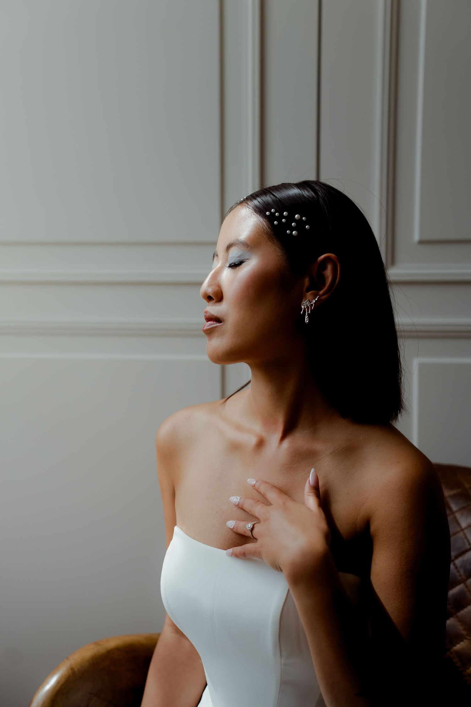 Close-up portrait of Asian bride with pearl hair pins, crystal ear cuff, and engagement ring in soft light.