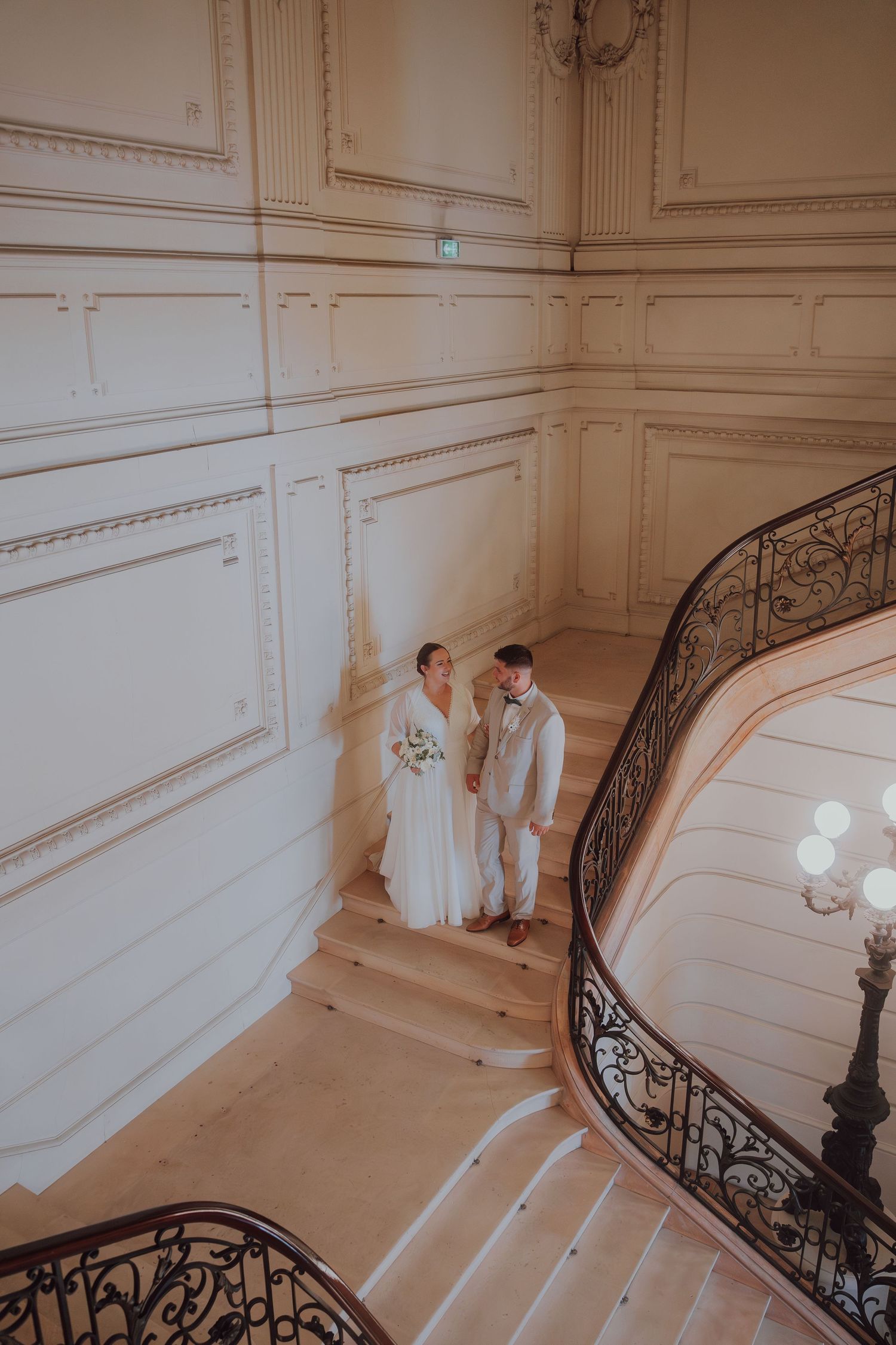 Aerial view of bride and groom holding hands on an ornate curved staircase in a elegant venue.
