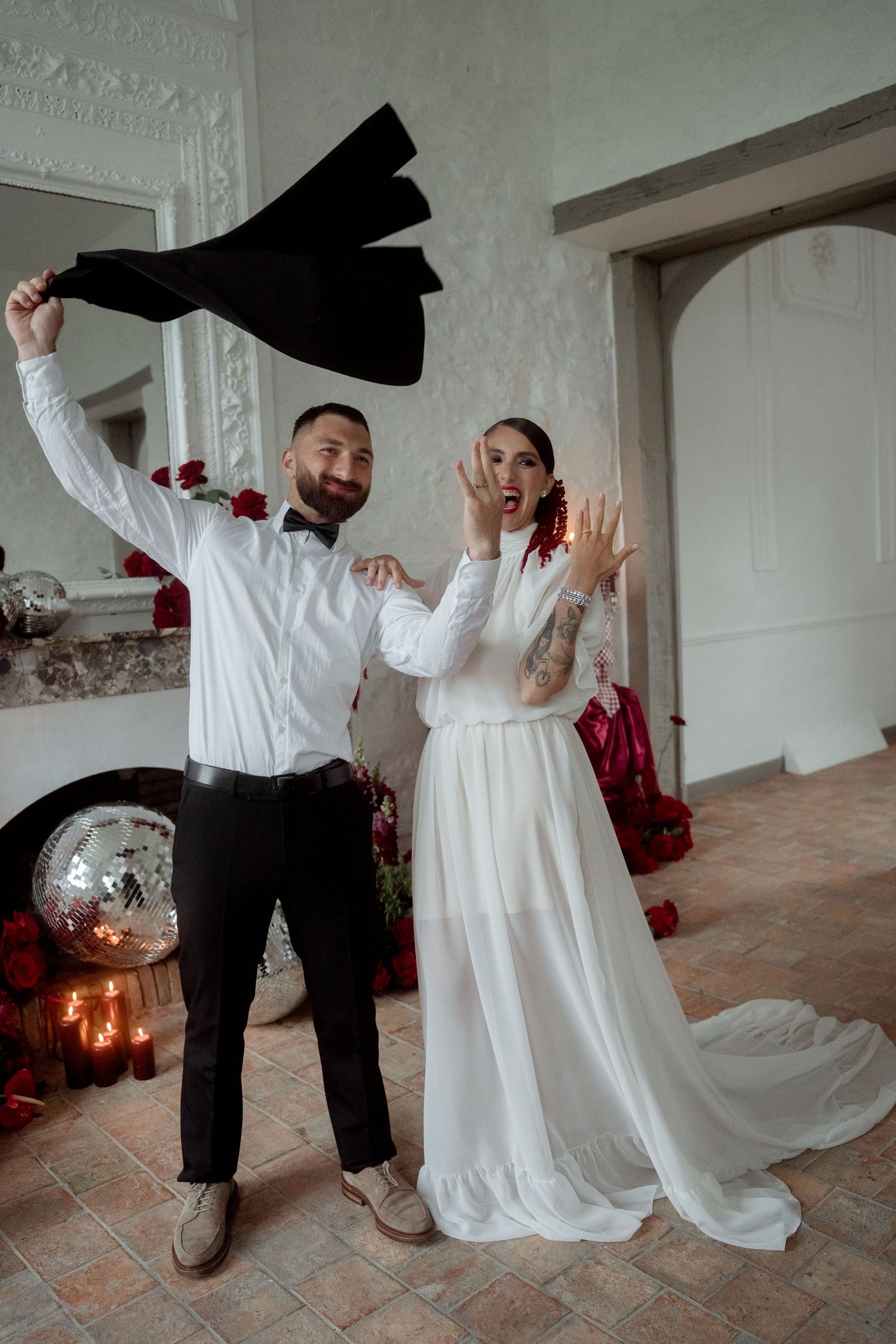 Joyful newlyweds celebrating after wedding ceremony, bride showing rings while groom waves jacket.