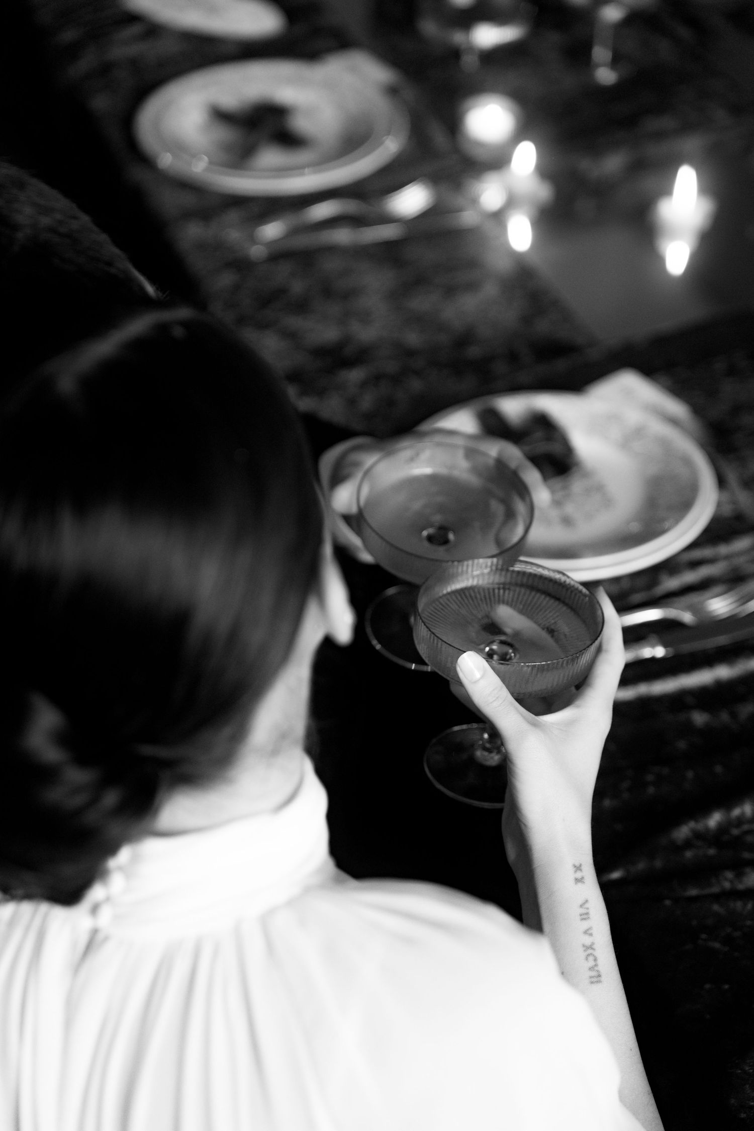 Black and white close-up of bride holding cocktail glass at candlelit wedding reception table.