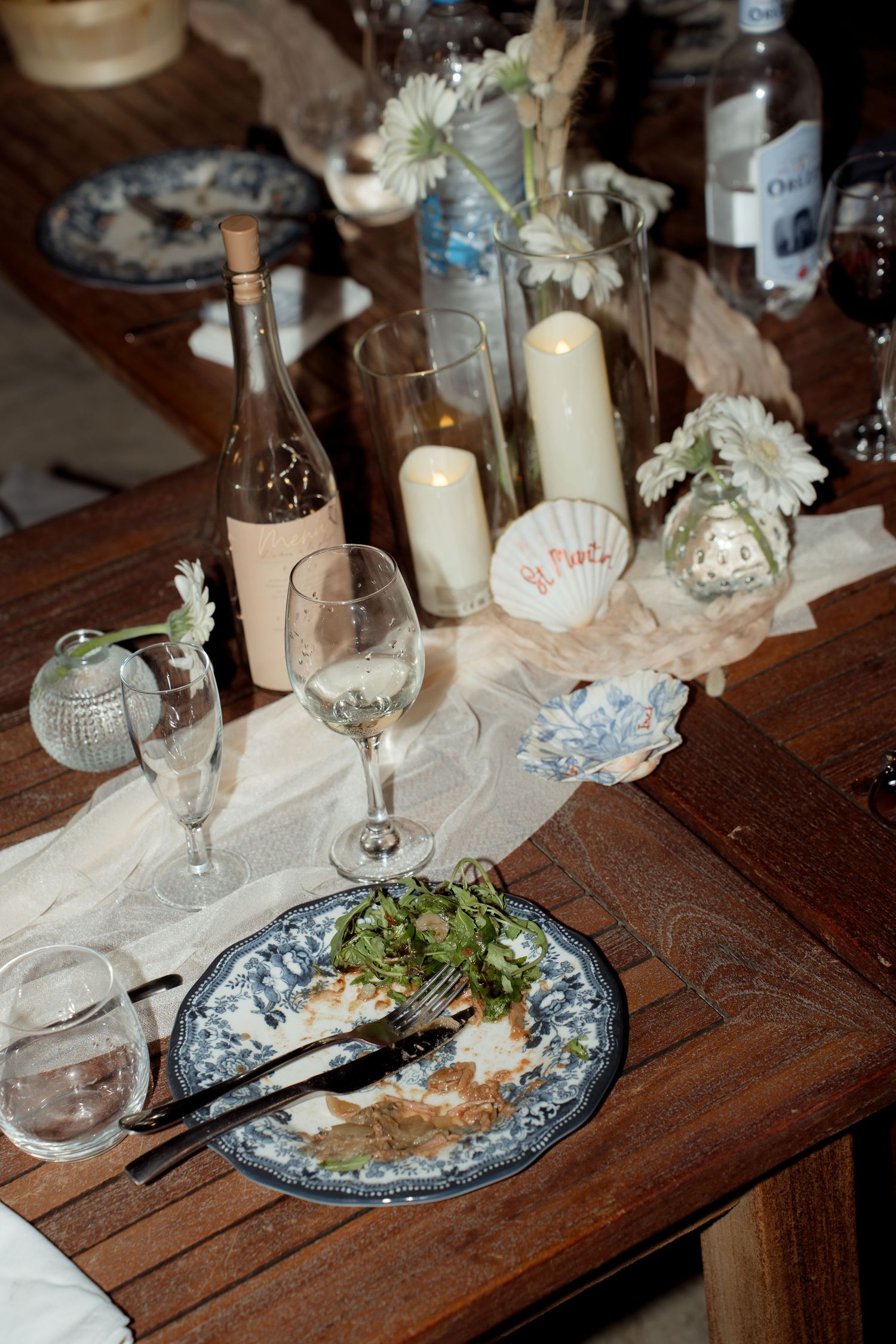 Elegant wedding table setting with candles, white flowers, wine glasses, and blue patterned plates.