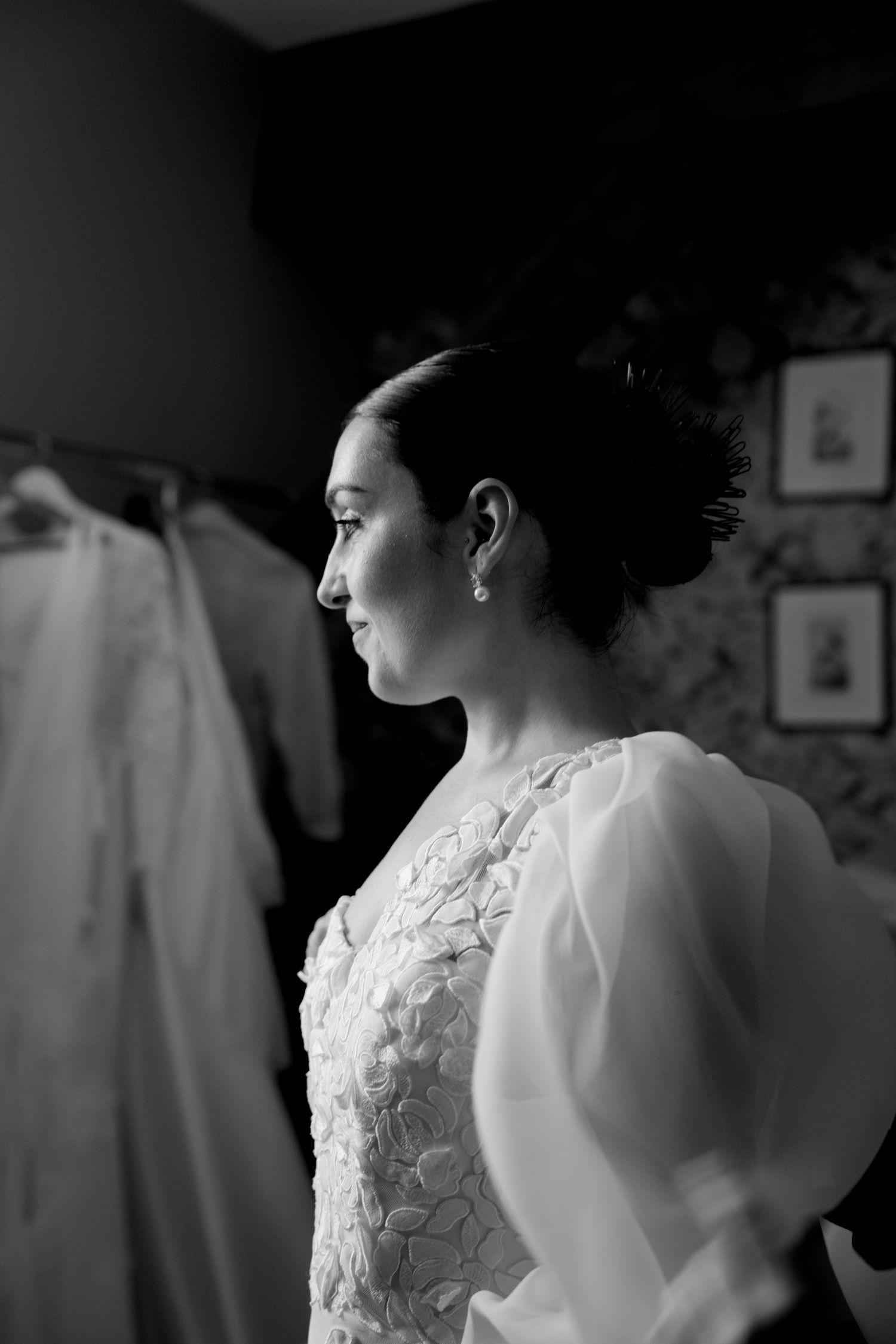 Black and white portrait of bride in lace wedding dress with updo hairstyle and pearl earrings during wedding preparations.