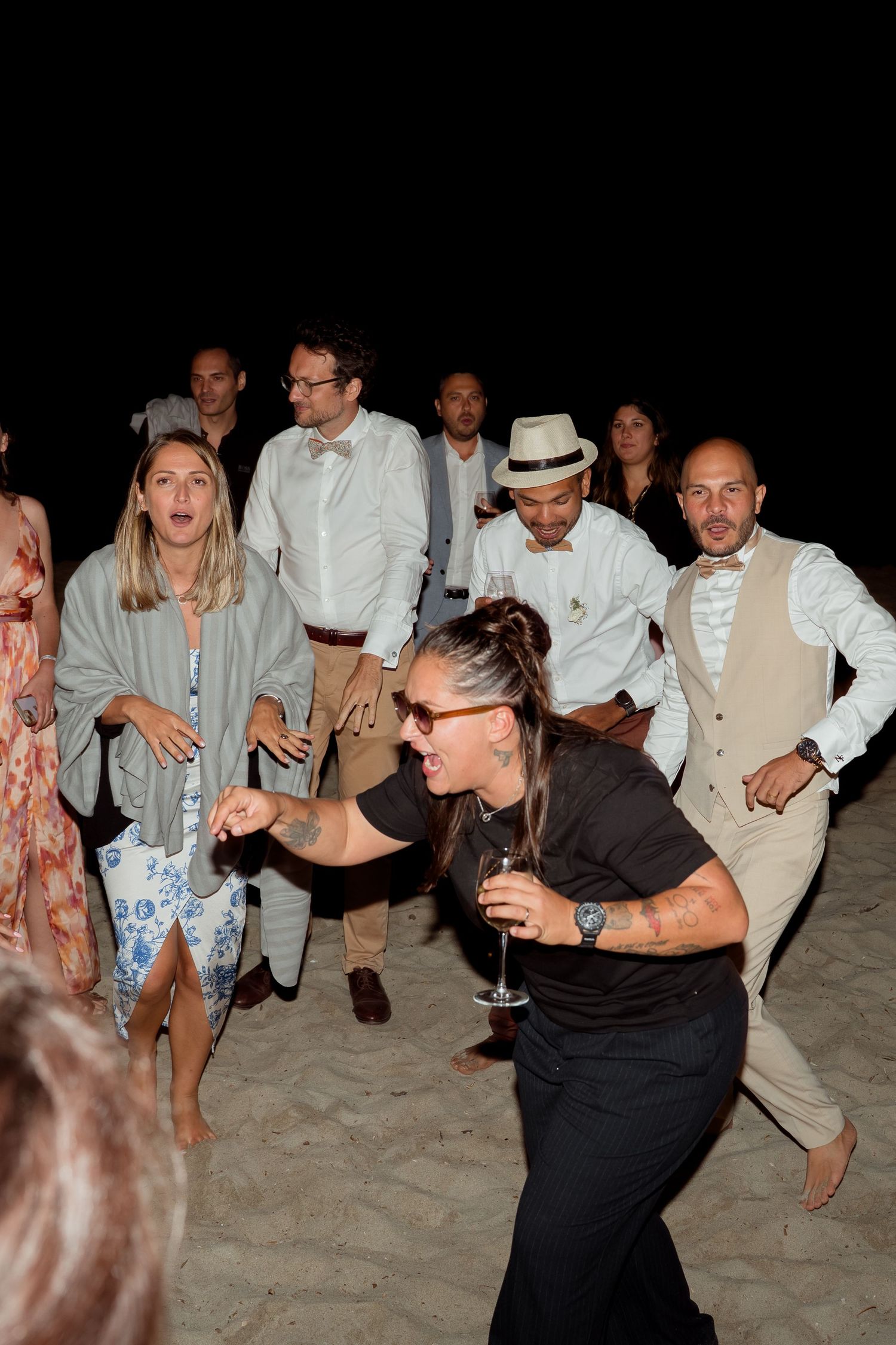 Wedding guests dancing energetically on a sandy beach at night.