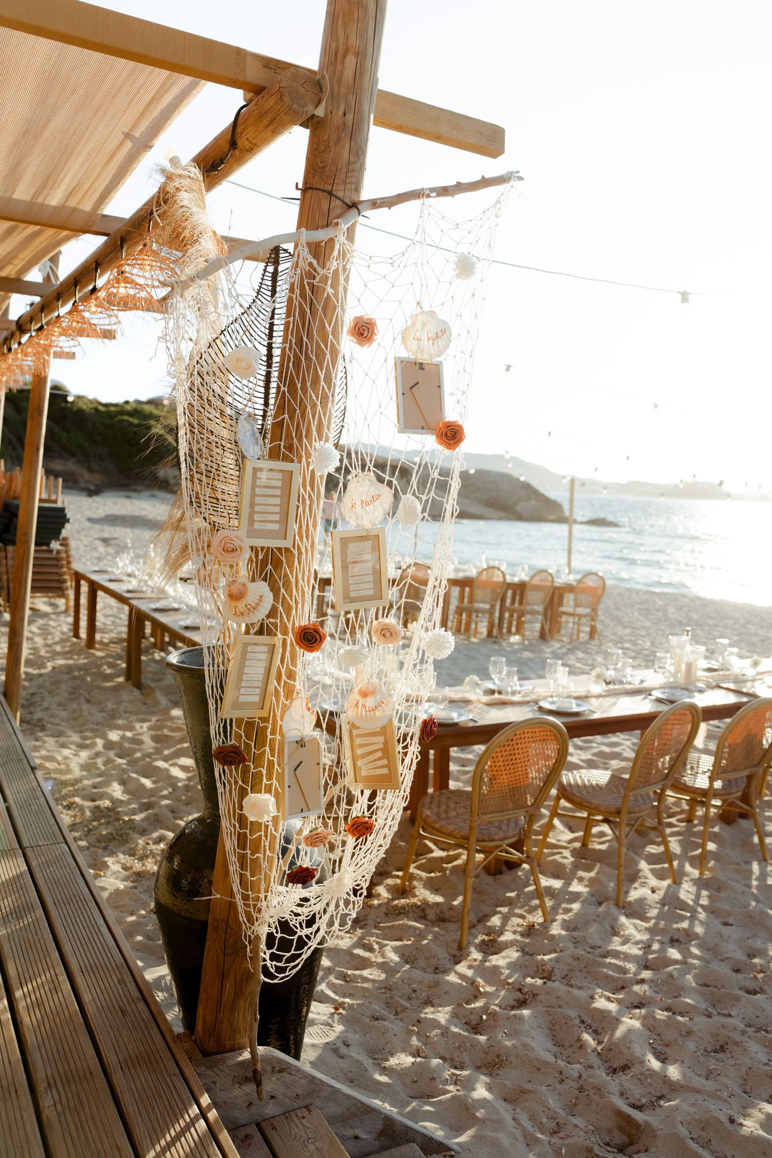Nautical beach wedding reception setup with fishing net seating chart, dreamcatchers, and ocean backdrop.