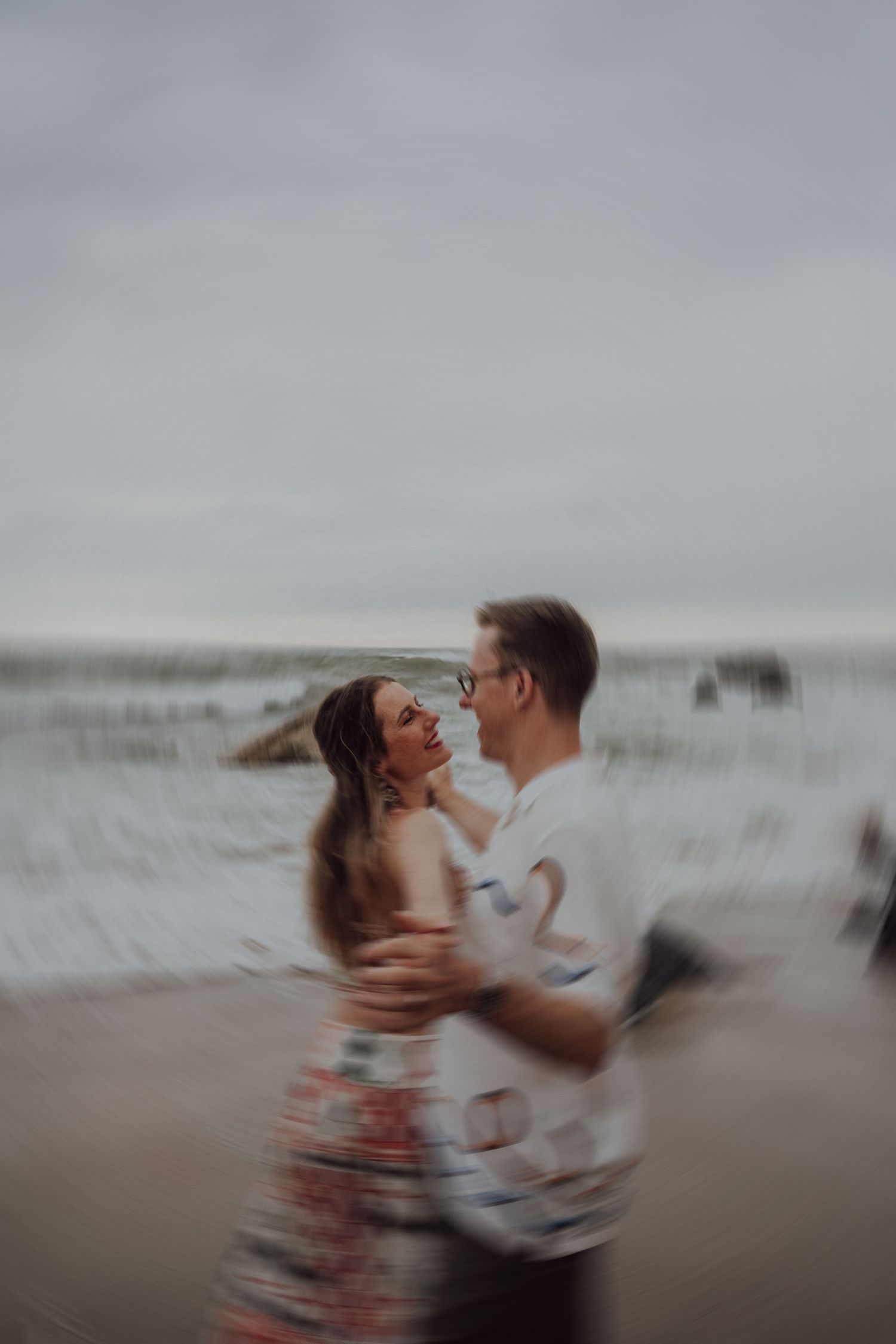 Blurred motion photo of couple dancing and embracing on beach with ocean backdrop.
