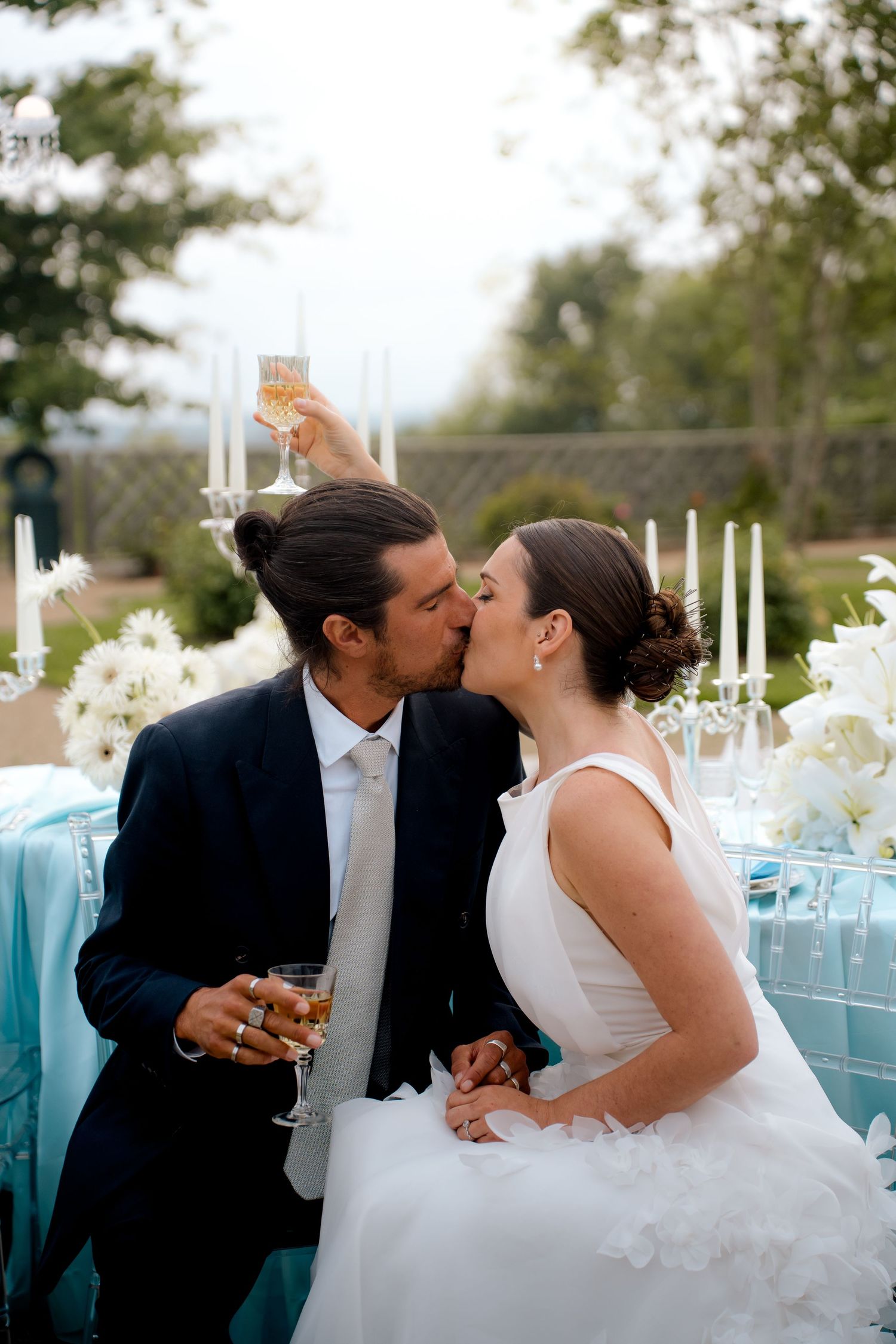Bride and groom kissing while holding champagne glasses at elegant tiffany blue outdoor reception.