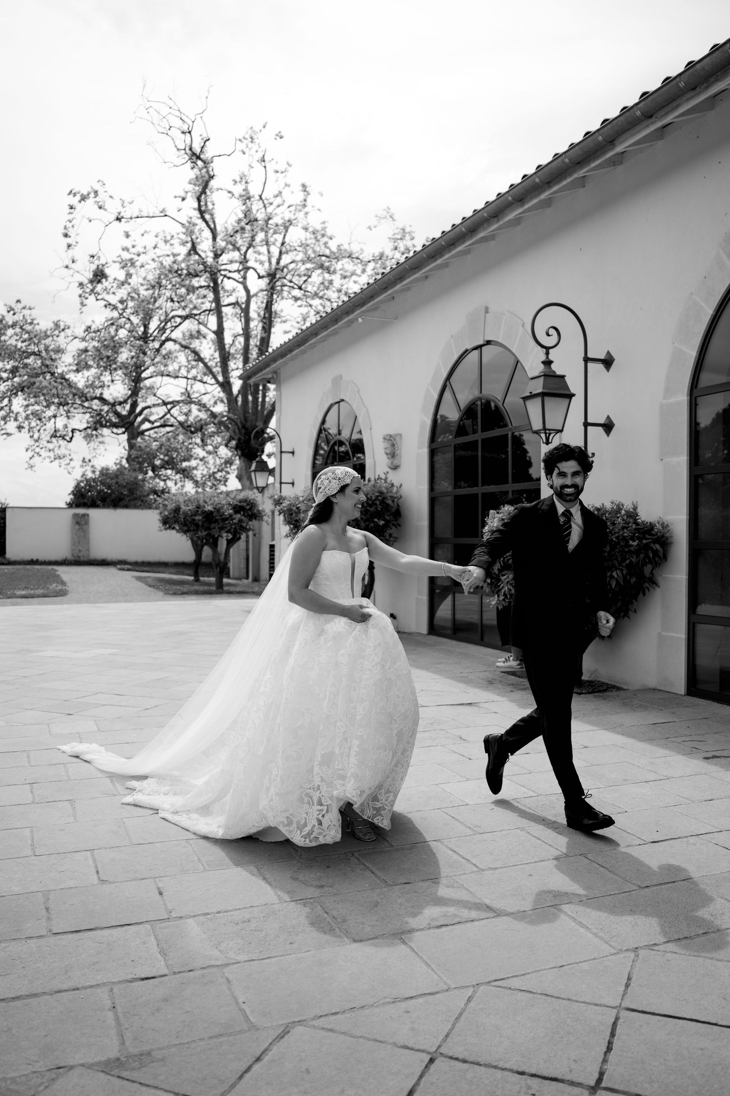 Black and white photo of bride and groom laughing and walking together outside a white wedding venue.