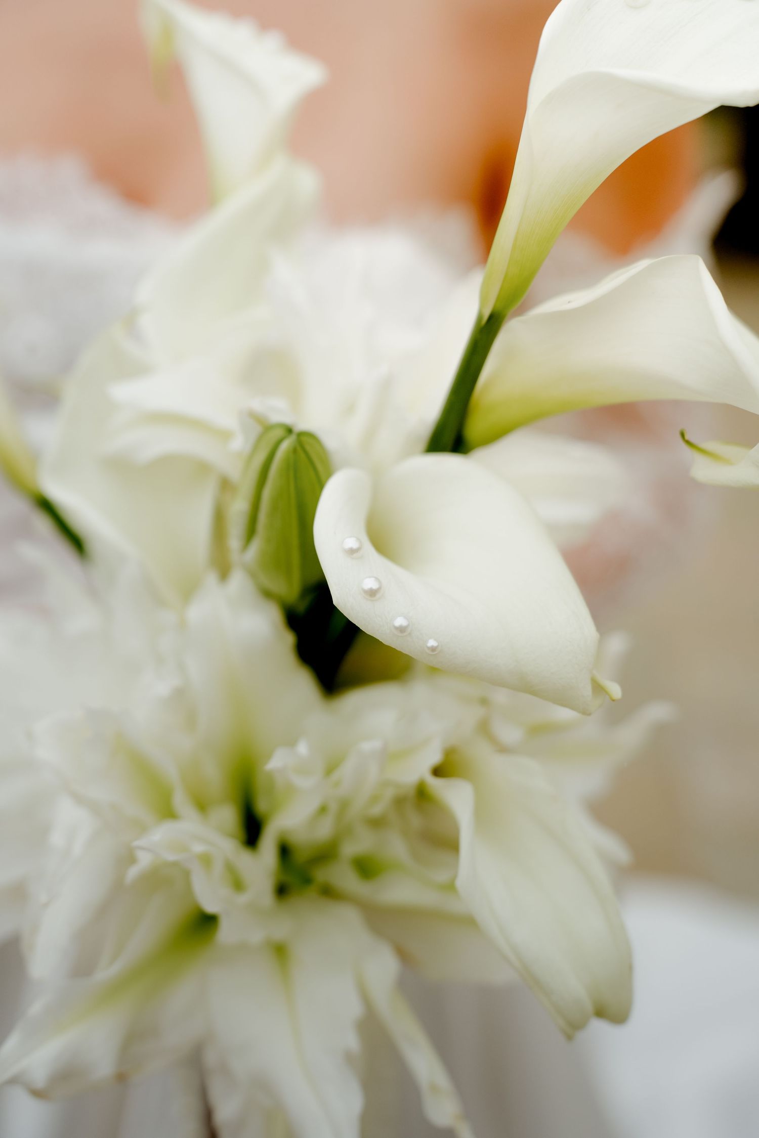 Close-up of elegant bridal bouquet featuring white calla lilies and lilies with pearl accents.