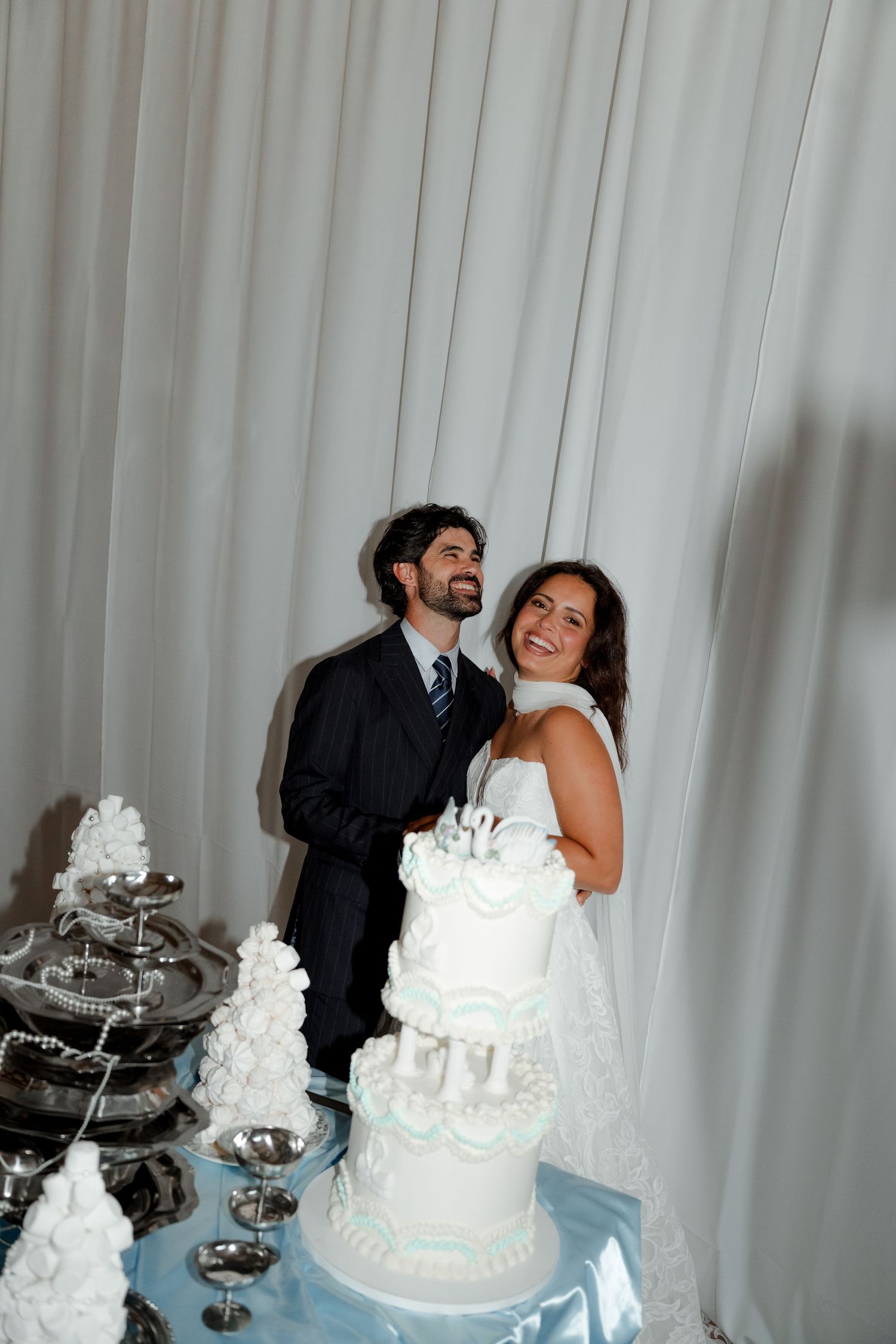 Smiling bride and groom standing beside their elegant white and blue tiered wedding cake at reception.