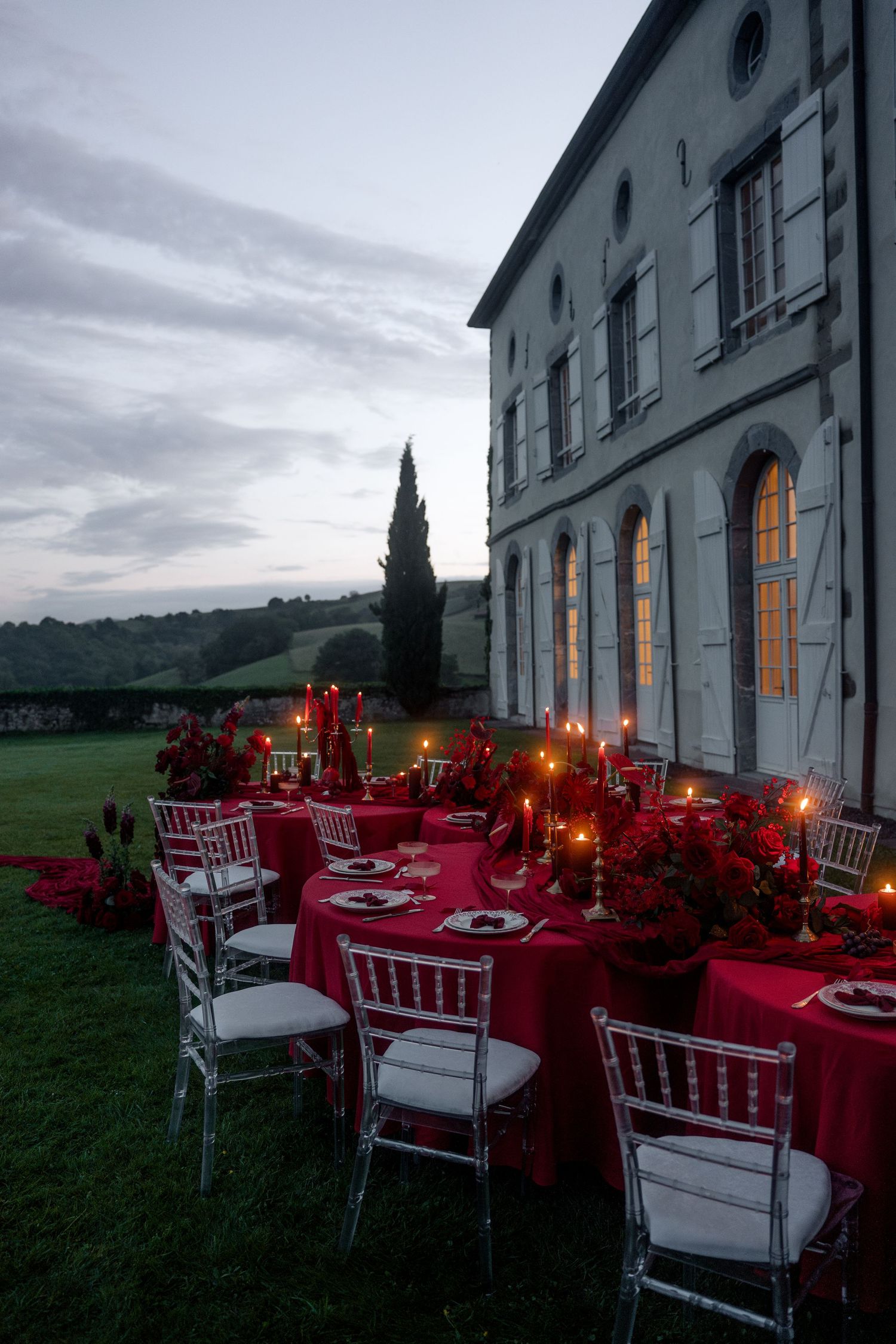Outdoor wedding reception table in red with candles and white chiavari chairs beside Italian villa at dusk.