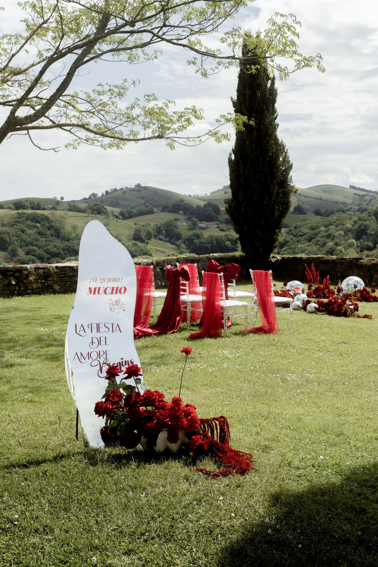 Outdoor wedding ceremony setup with red floral decorations, mirror balls, and rolling hills backdrop in Tuscany.