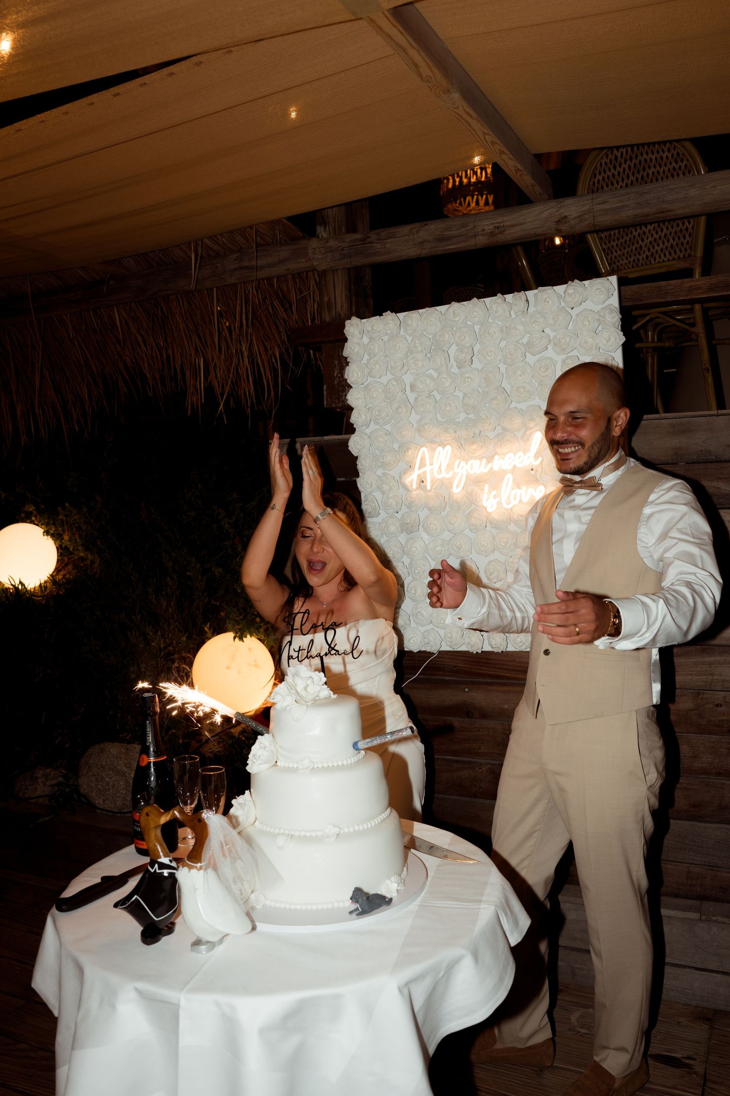 Bride and groom celebrating beside a white tiered wedding cake with sparklers.