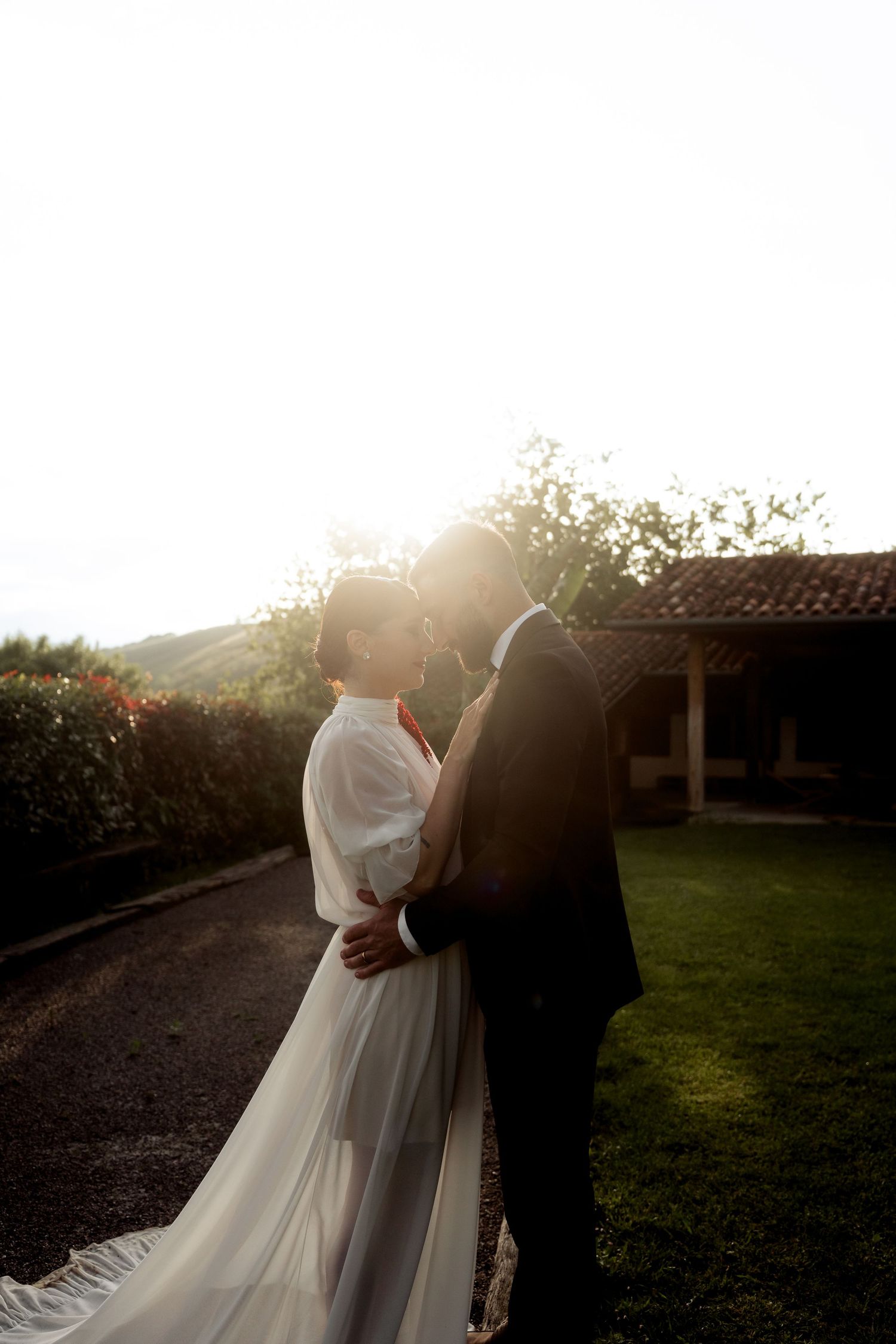 Bride and groom share intimate kiss bathed in golden sunset light in garden setting.