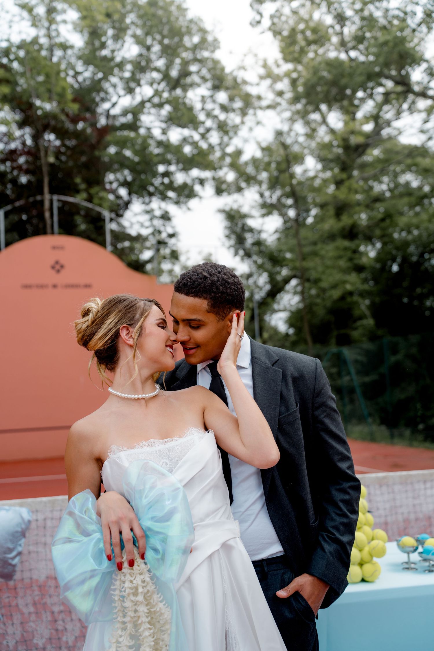 Interracial bride and groom sharing romantic moment on tennis court wedding venue.
