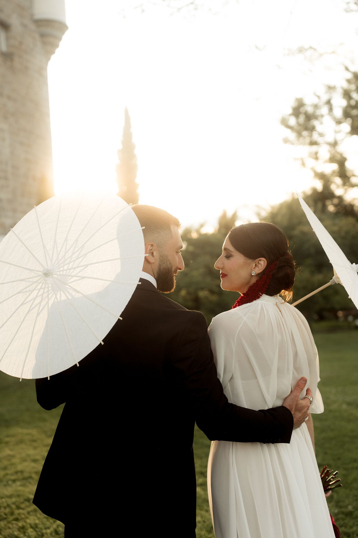 Elegant couple sharing an intimate moment with white parasols during a golden hour outdoor wedding.