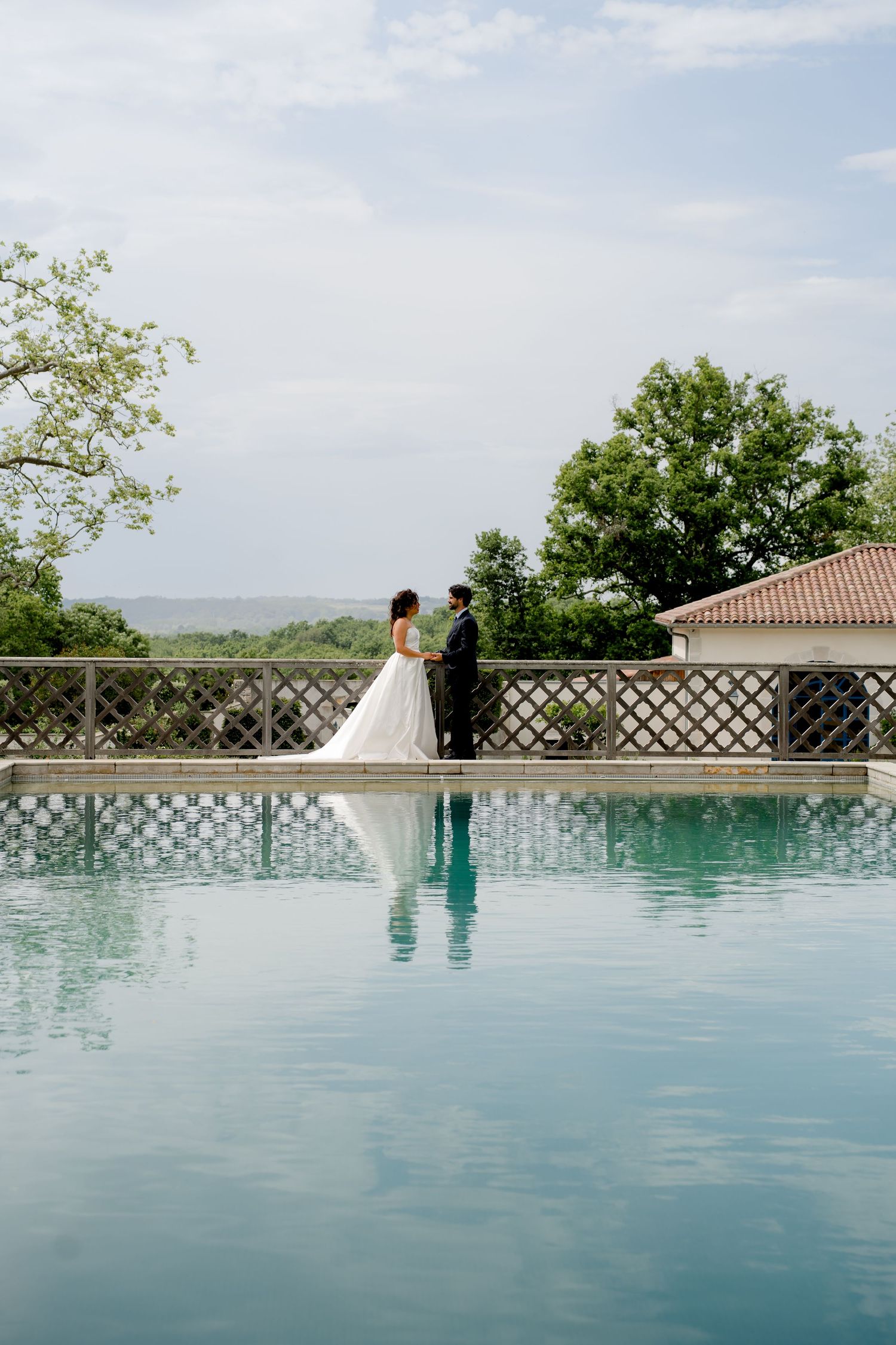 Bride and groom hold hands beside a stunning infinity pool with scenic countryside views on their wedding day.