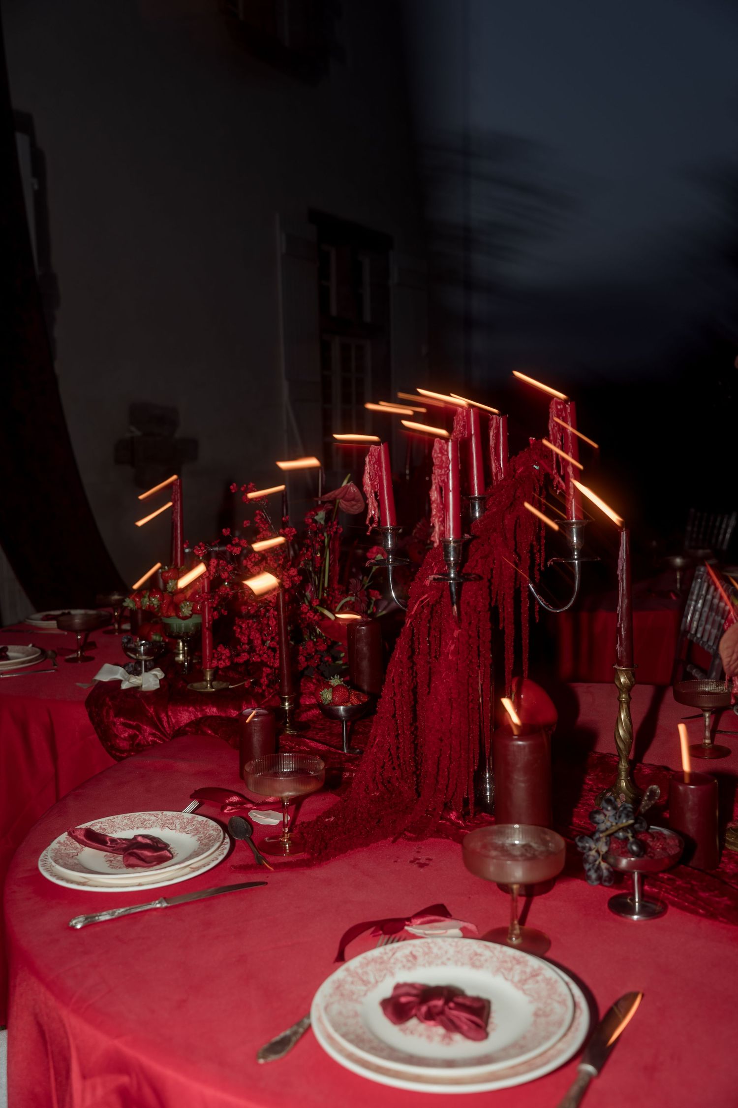 Dramatic red wedding table setting with glowing candelabras, red linens, and ornate place settings indoors.