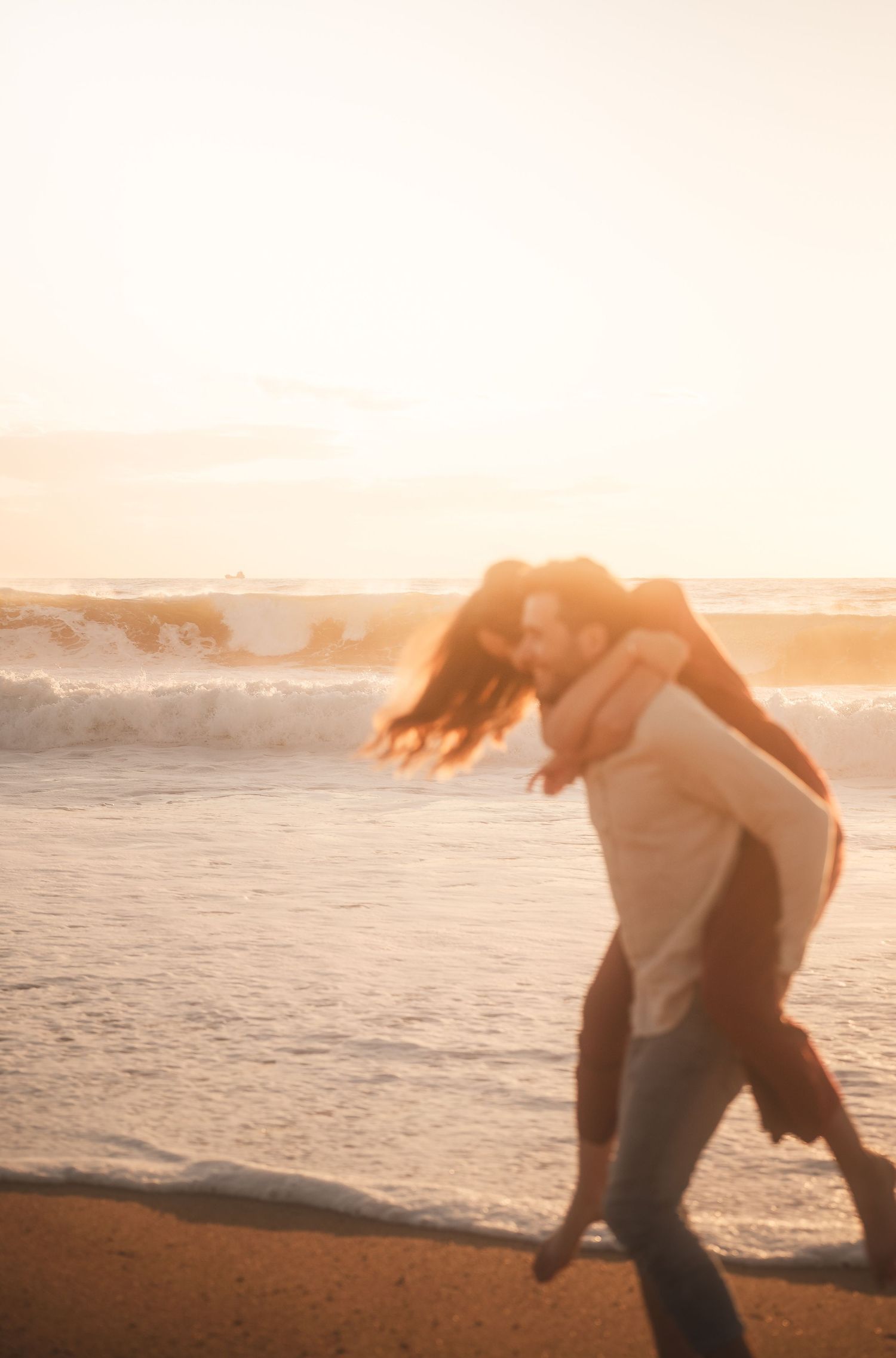 Couple sharing a romantic piggyback ride on the beach during a glowing golden sunset.