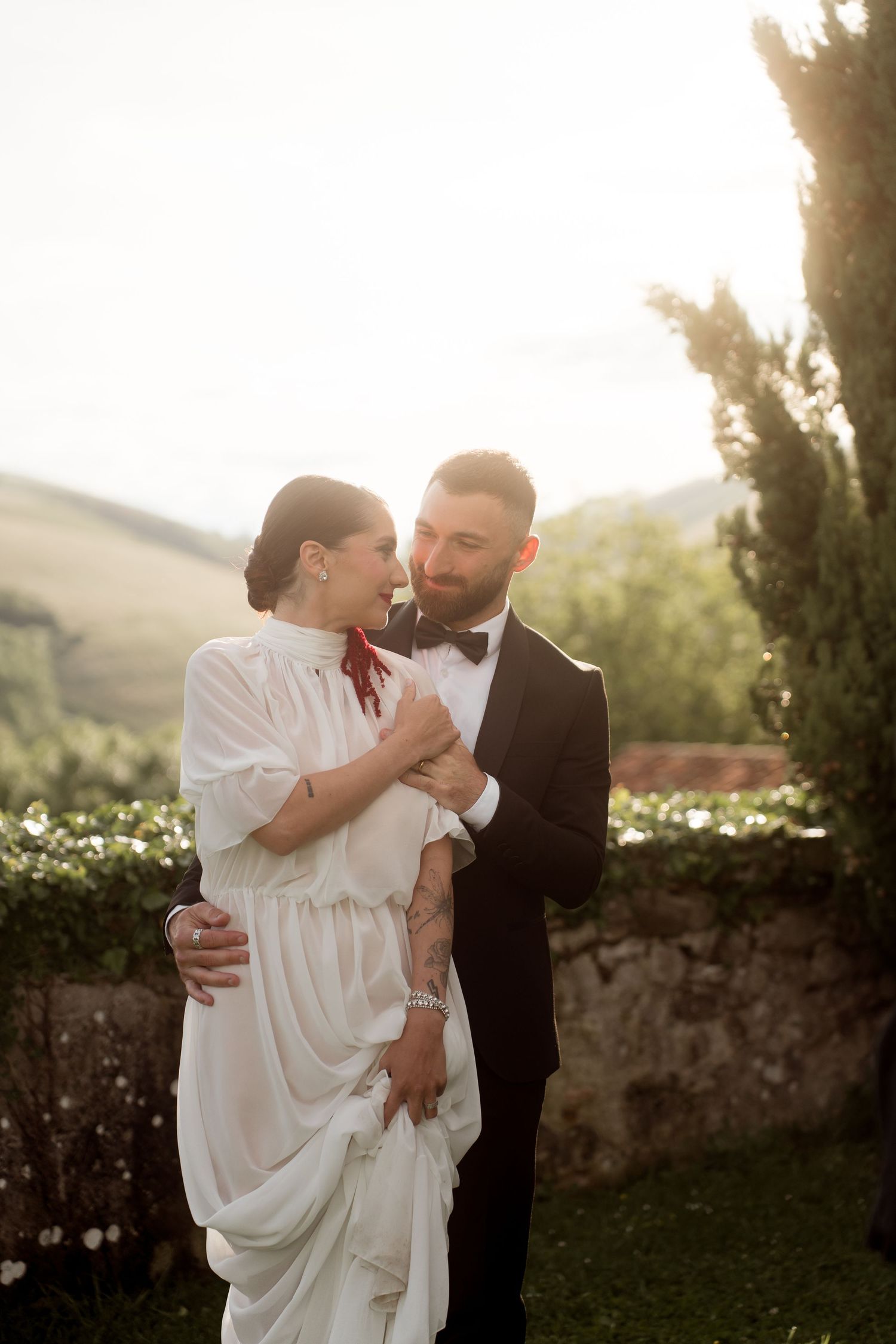 Elegant wedding couple embracing tenderly in warm sunset light with Tuscan hills backdrop.