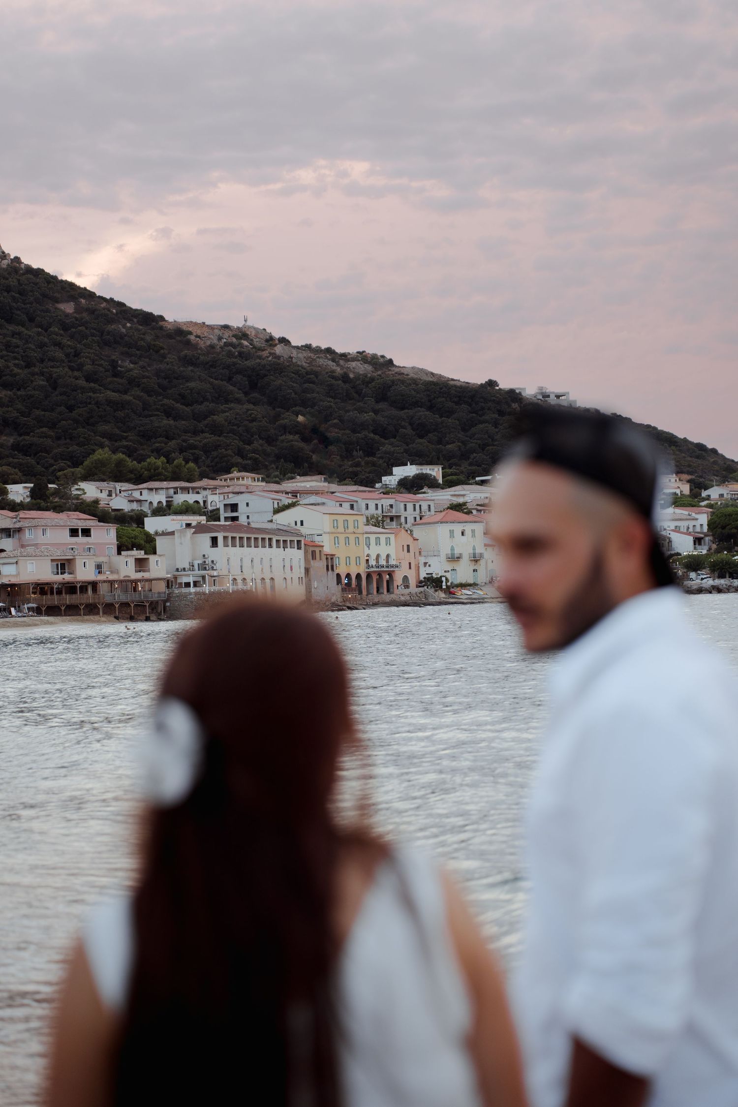 Couple standing out of focus looking at a picturesque coastal village across the water at sunset.