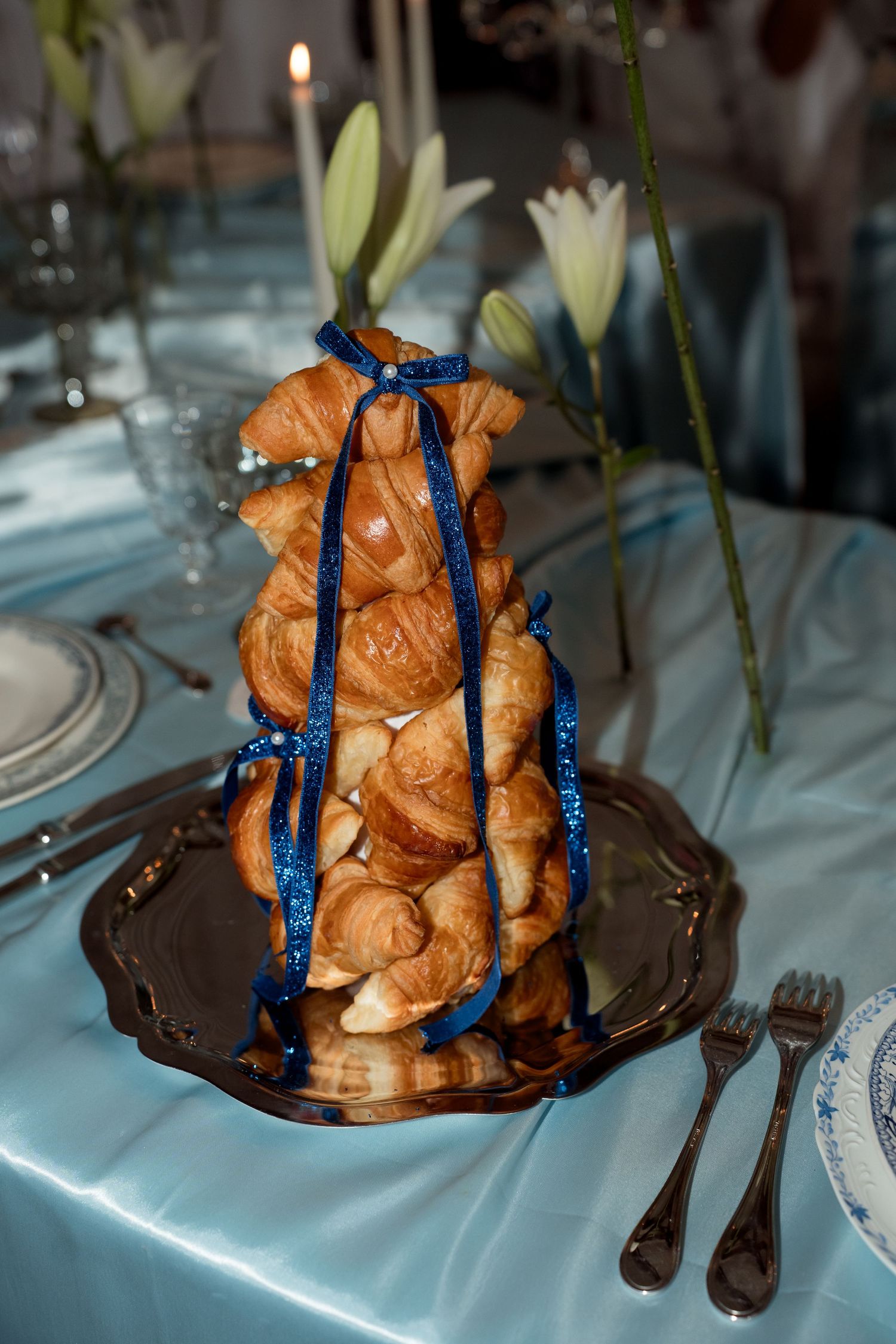Elegant croquembouche tower decorated with blue ribbon on a silver platter at a wedding reception.