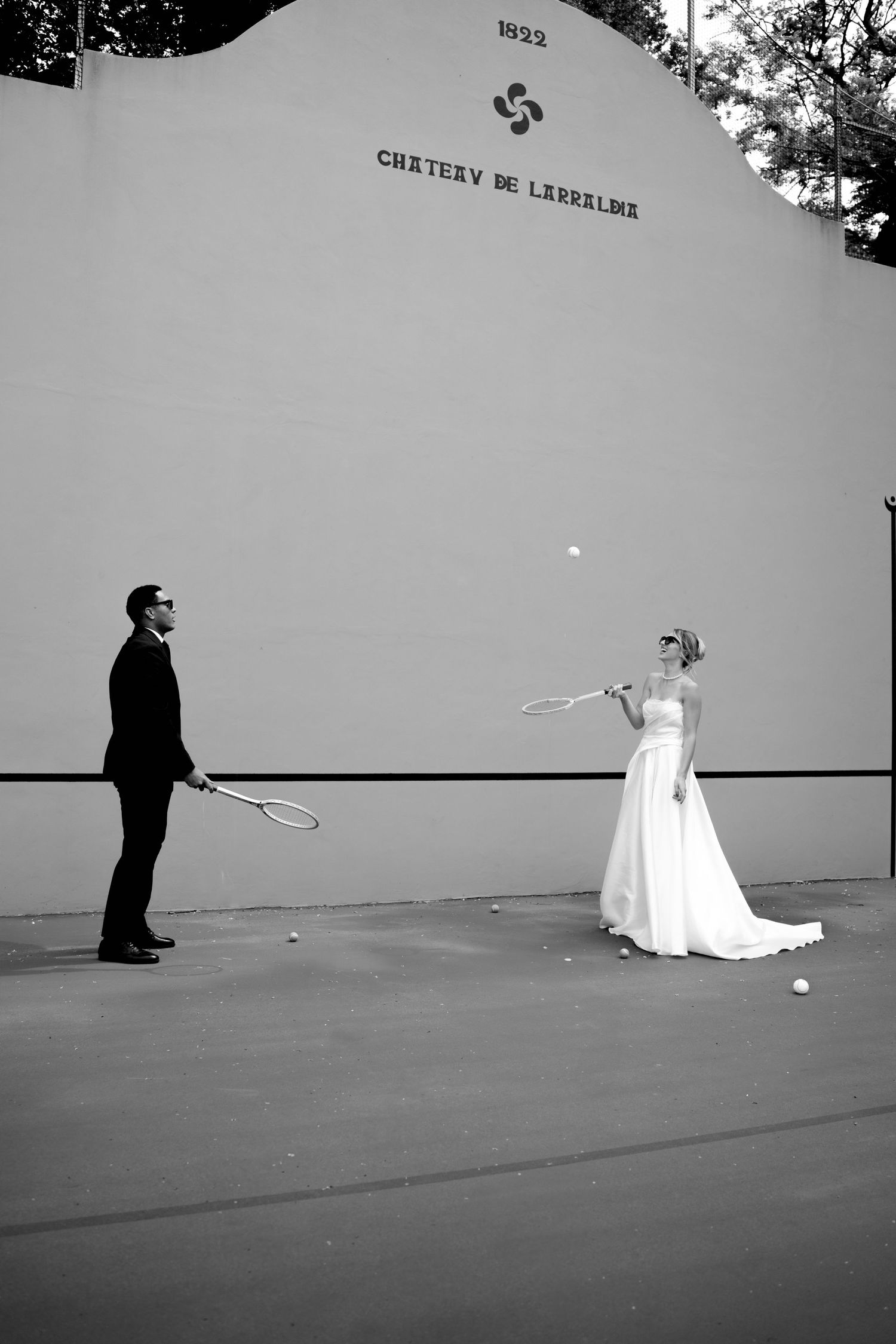 Black and white photo of bride and groom playing tennis at Chateau de Larraldia court.