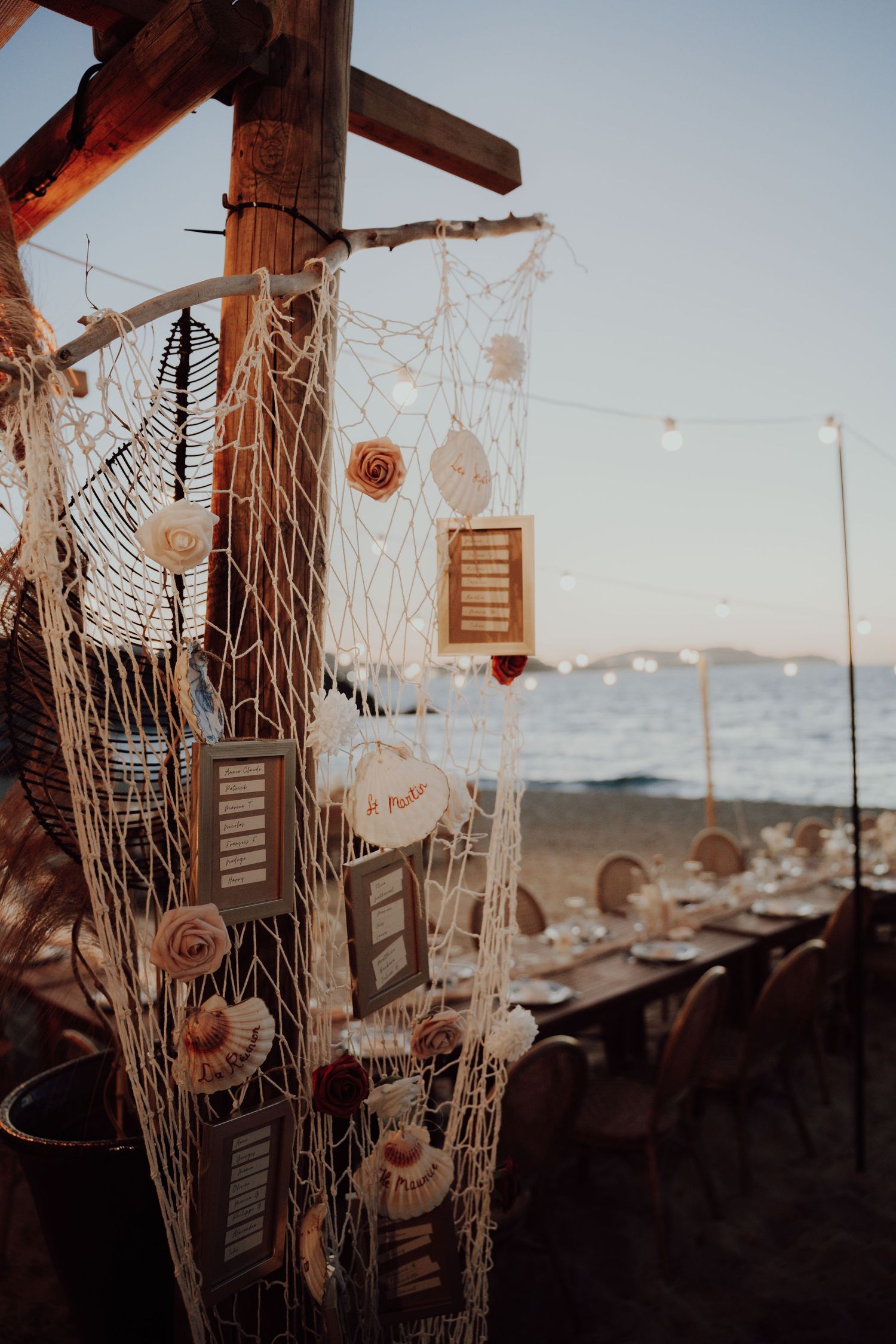 Decorative fishing net with seashells and framed table cards at a seaside wedding reception at sunset.