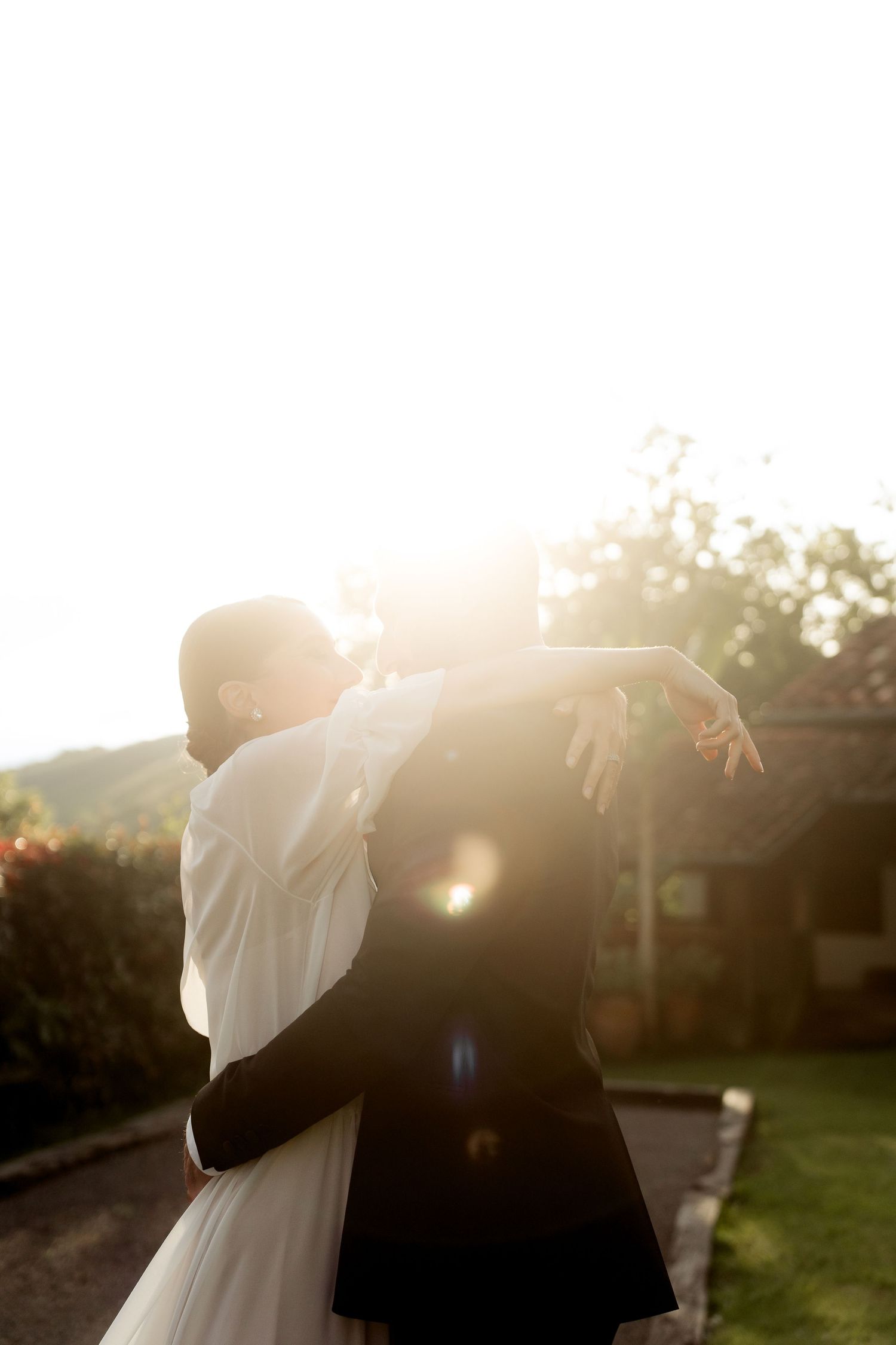 Bride and groom share tender embrace in brilliant golden sunset light during wedding shoot.