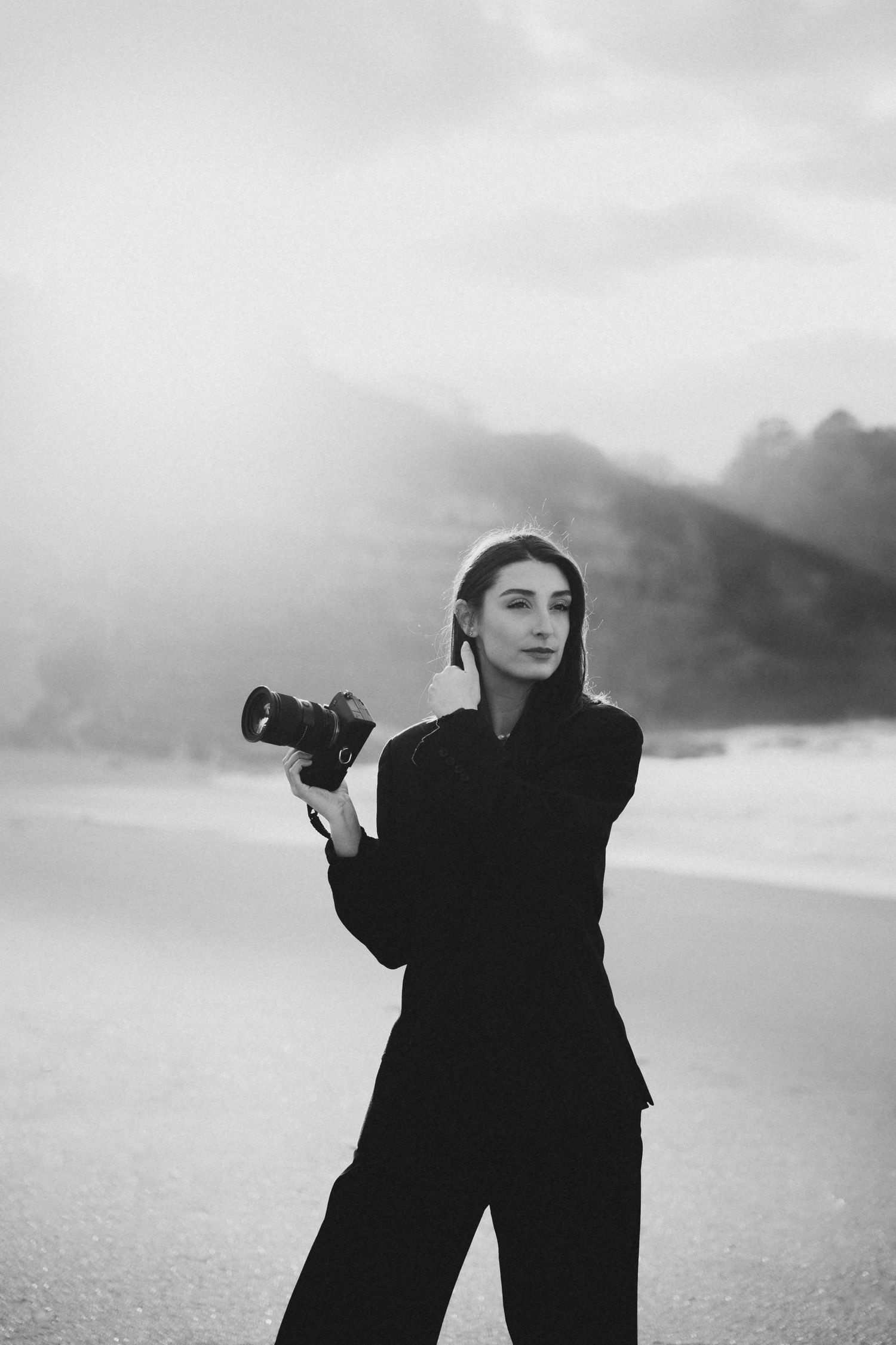Black and white portrait of female photographer holding camera on misty beach.