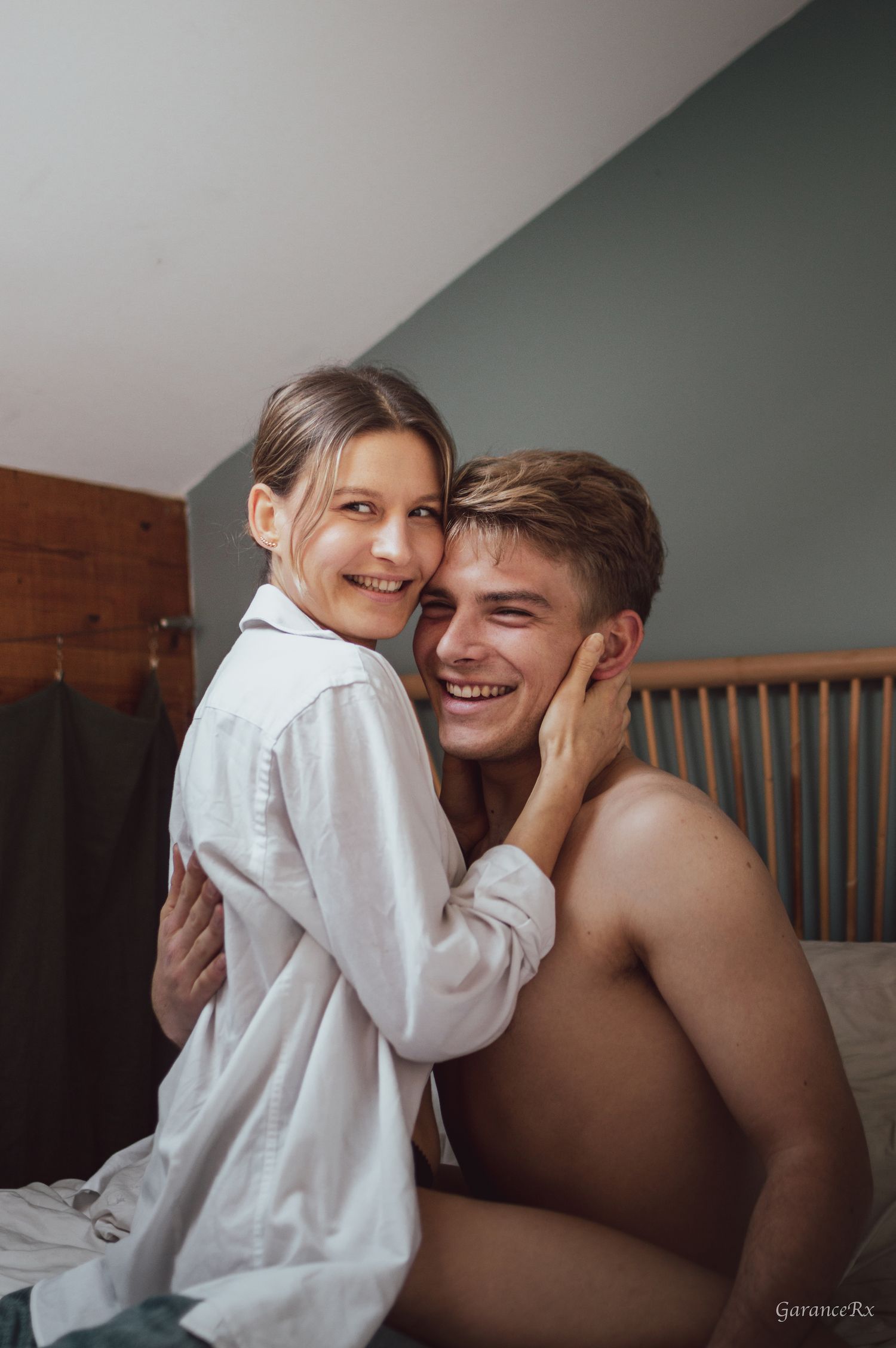 Happy couple smiling and embracing on a bed in a cozy room with wooden accents.