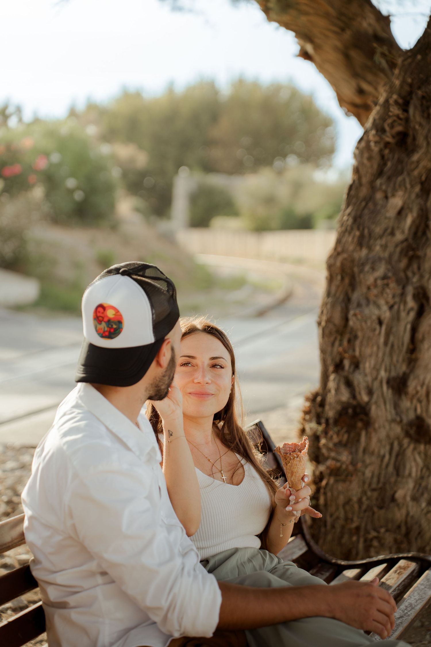 Couple sitting on a bench under a tree at sunset, woman holding an ice cream cone.