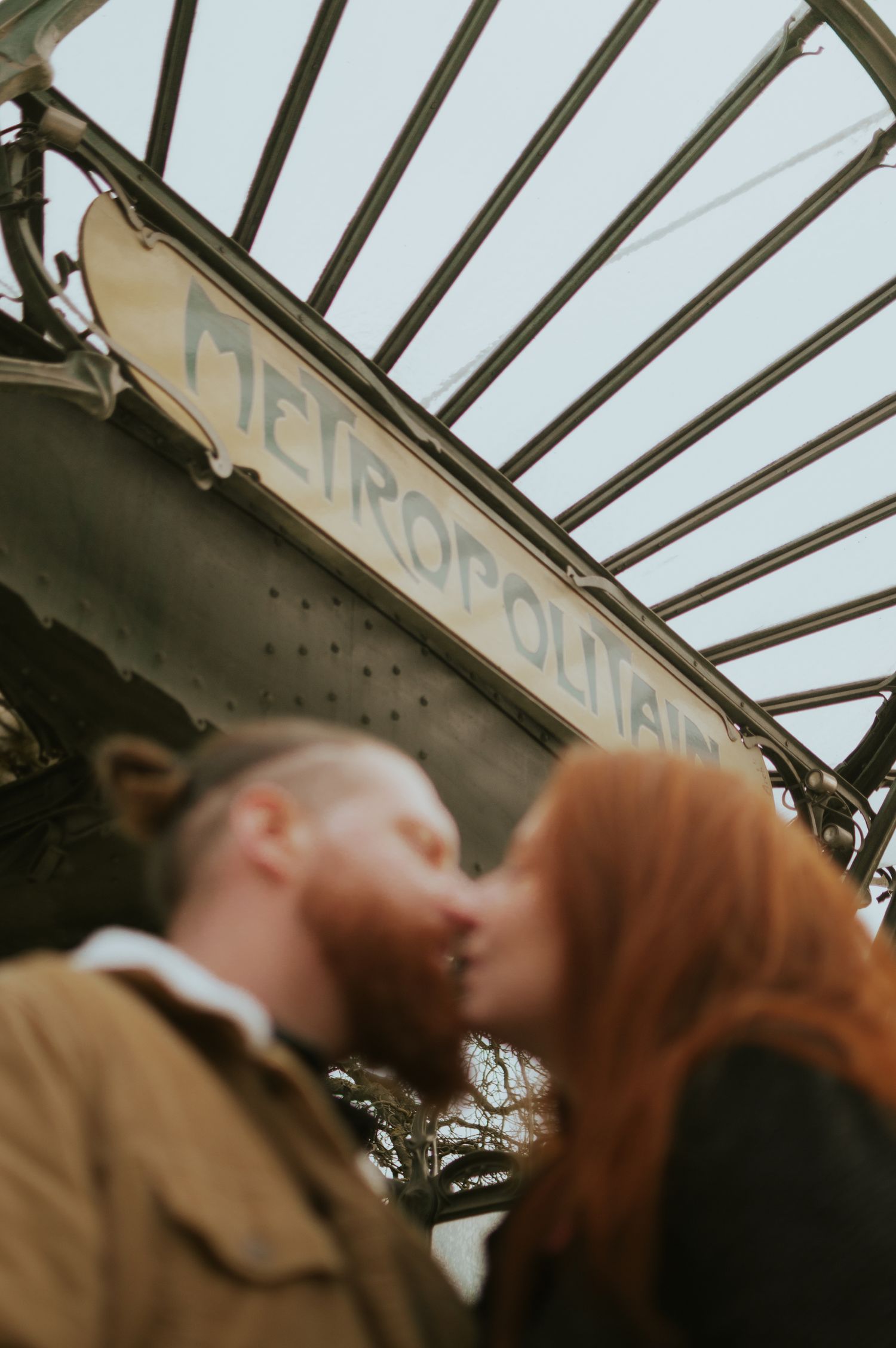 Couple sharing a kiss in front of a Paris Metropolitain metro sign entrance.