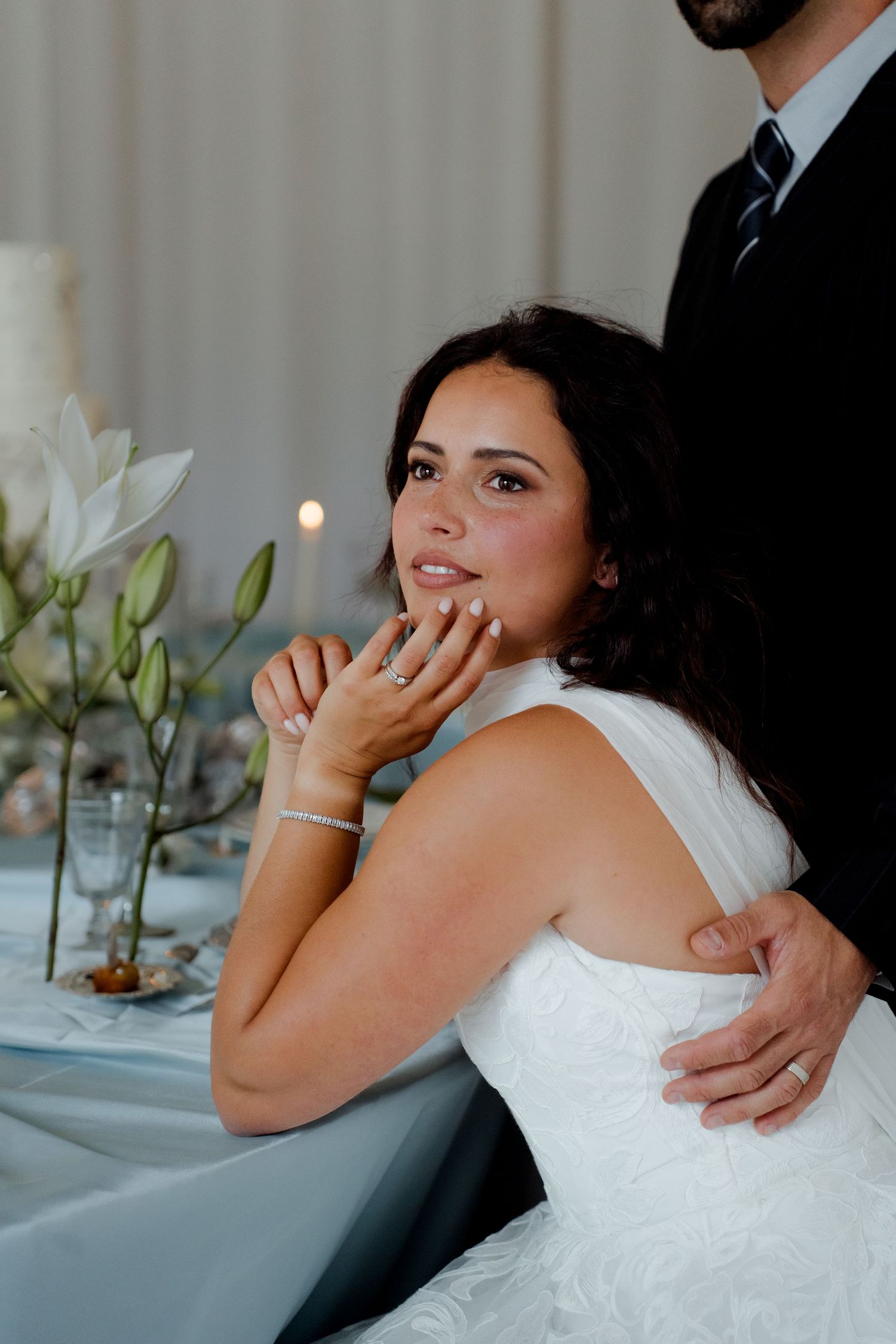 Radiant bride gazing upward at wedding table adorned with white lilies and candles.