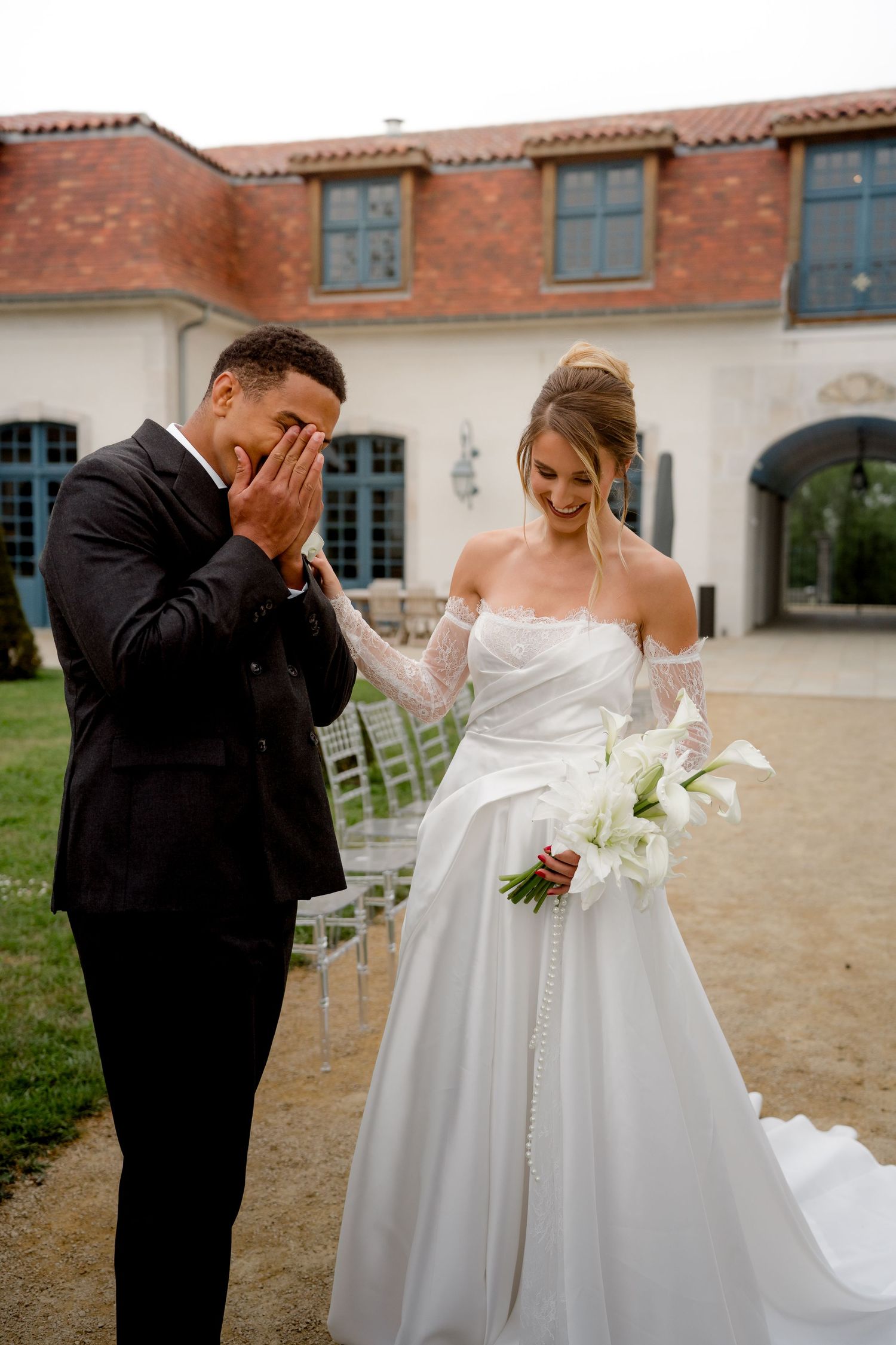 Emotional groom covering face while bride laughs during outdoor first look wedding moment.