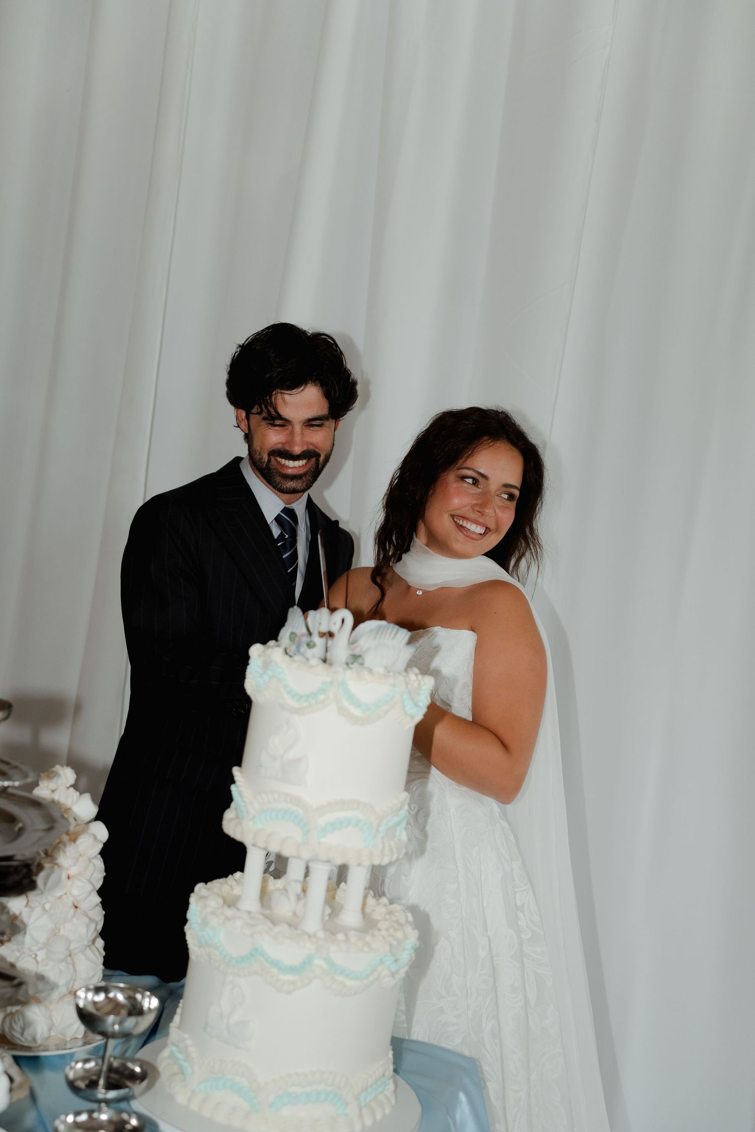 Joyful bride and groom smiling while cutting their white and blue tiered wedding cake.