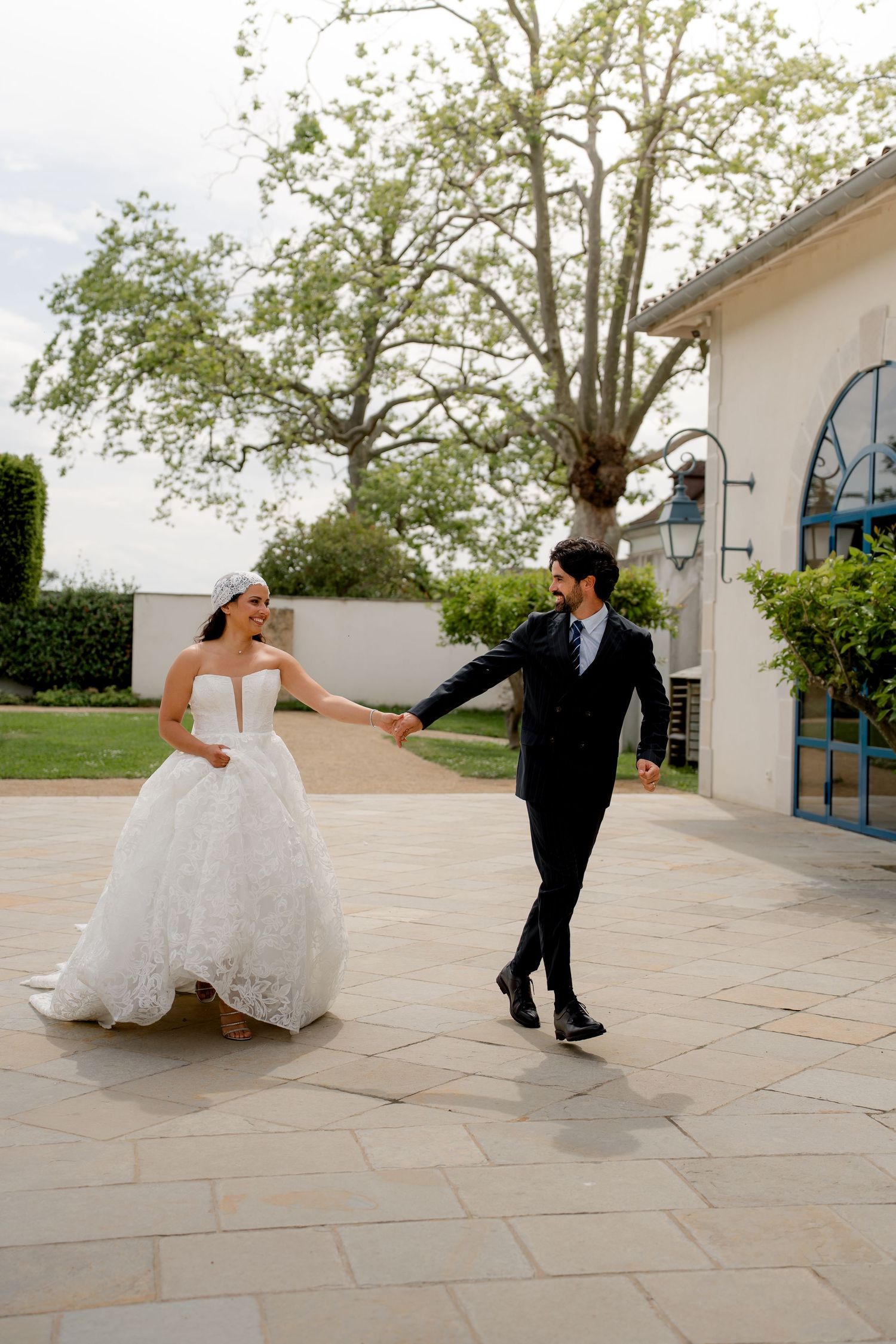 Joyful bride in ball gown and groom dancing on stone terrace surrounded by lush garden greenery.