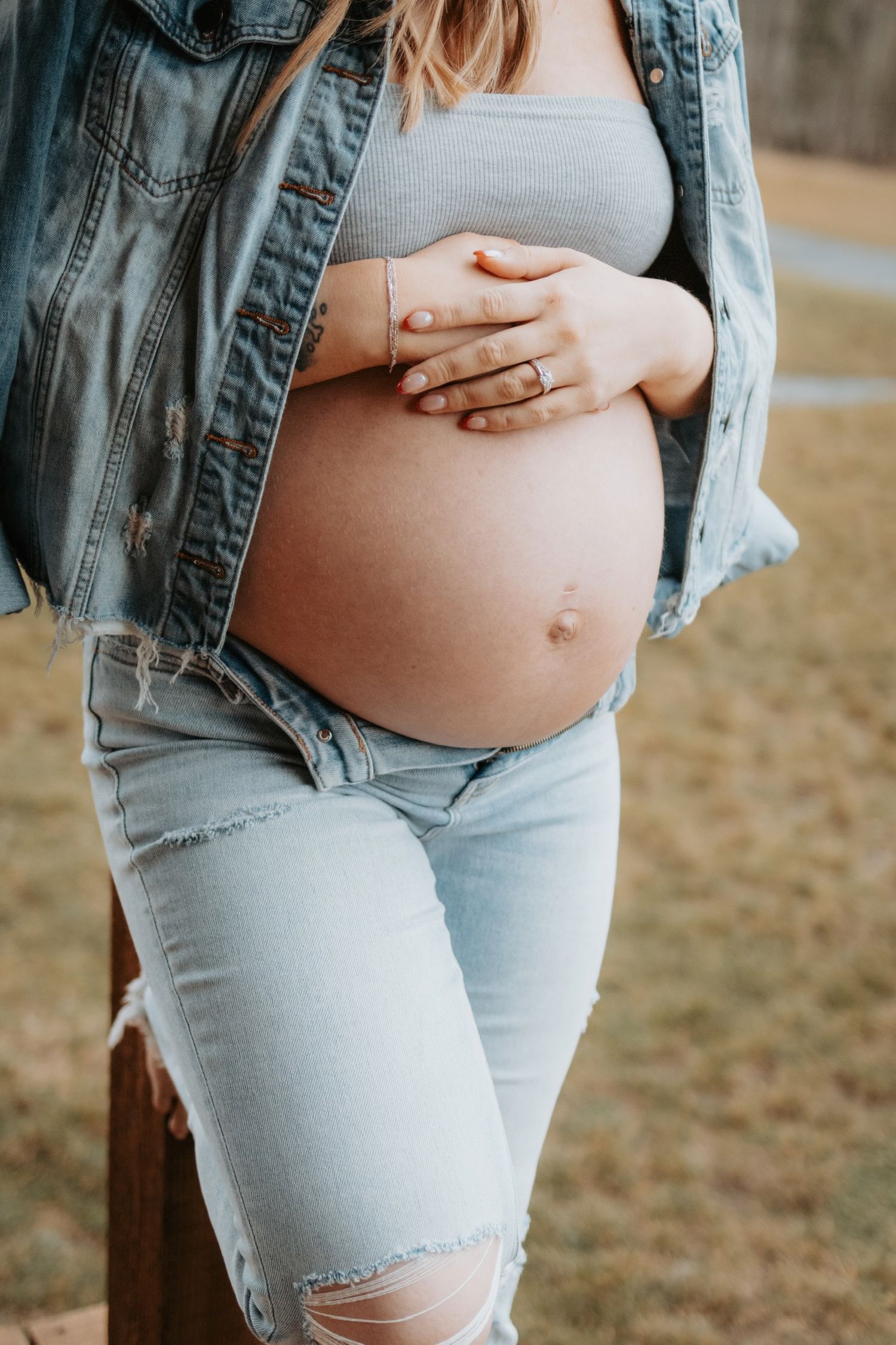Maternity photo showing pregnant belly with hands resting on bump, wearing denim jacket.