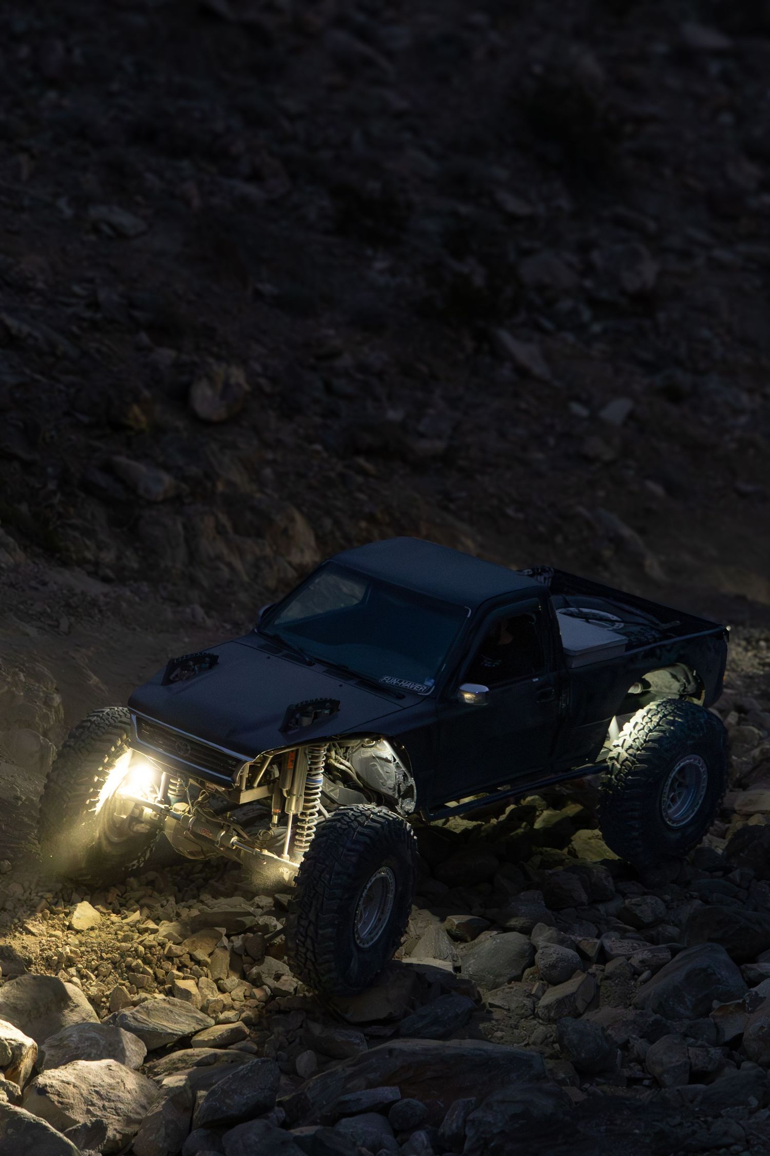 Off-road vehicle navigating rocky terrain at night with headlights illuminating the dark landscape.