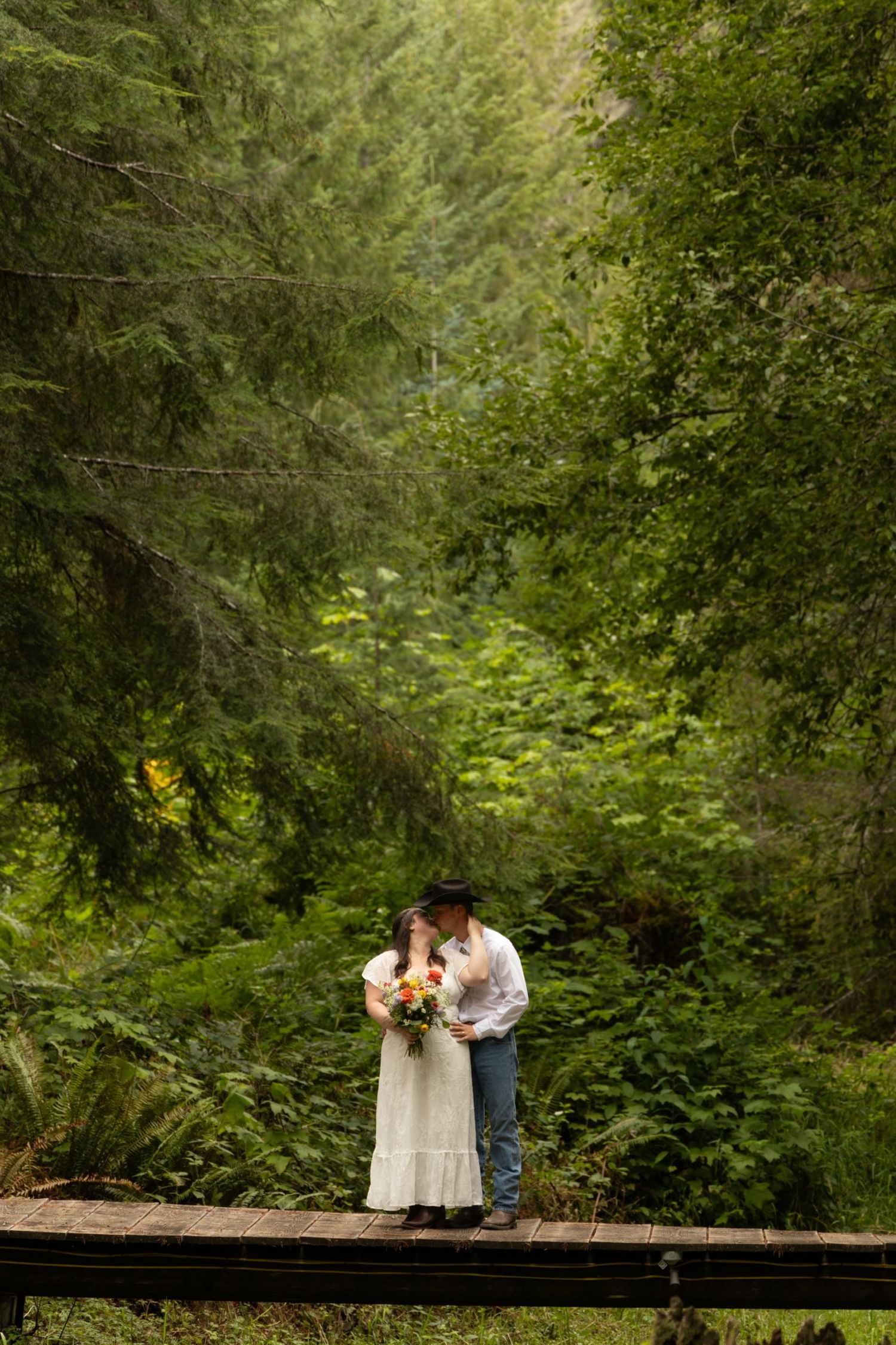 A romantic wedding portrait on a wooden bridge surrounded by lush green forest.