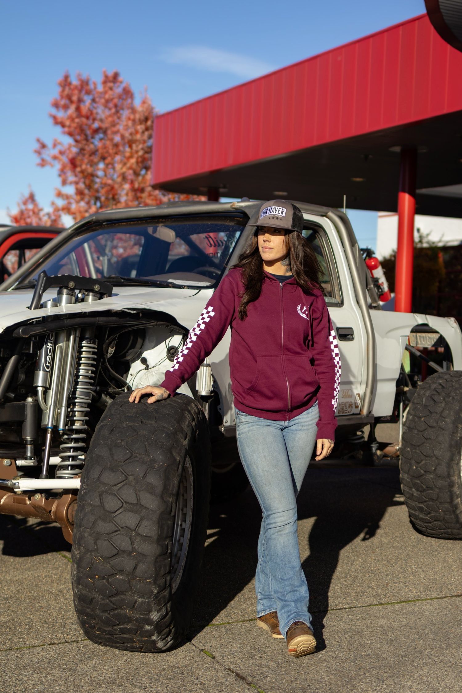 Large off-road tires and vehicle parts displayed with burgundy clothing in outdoor setting.