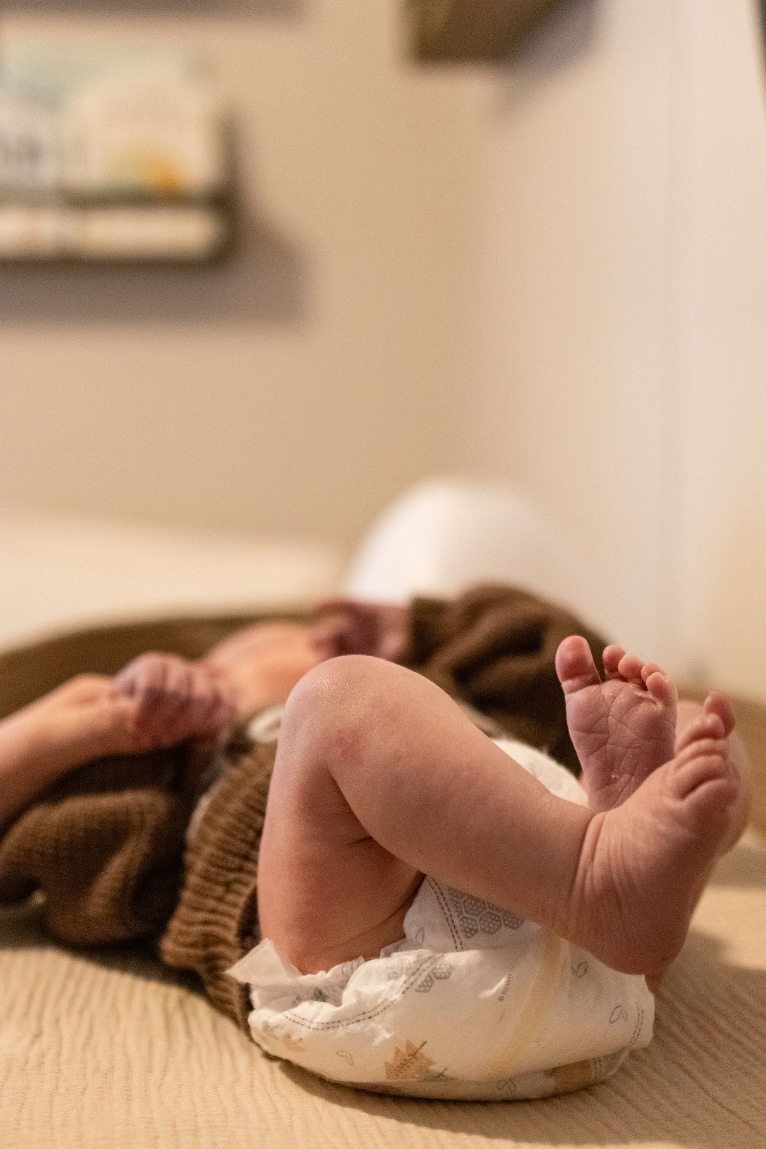 Close-up of baby's tiny feet and diaper while resting on brown blanket.