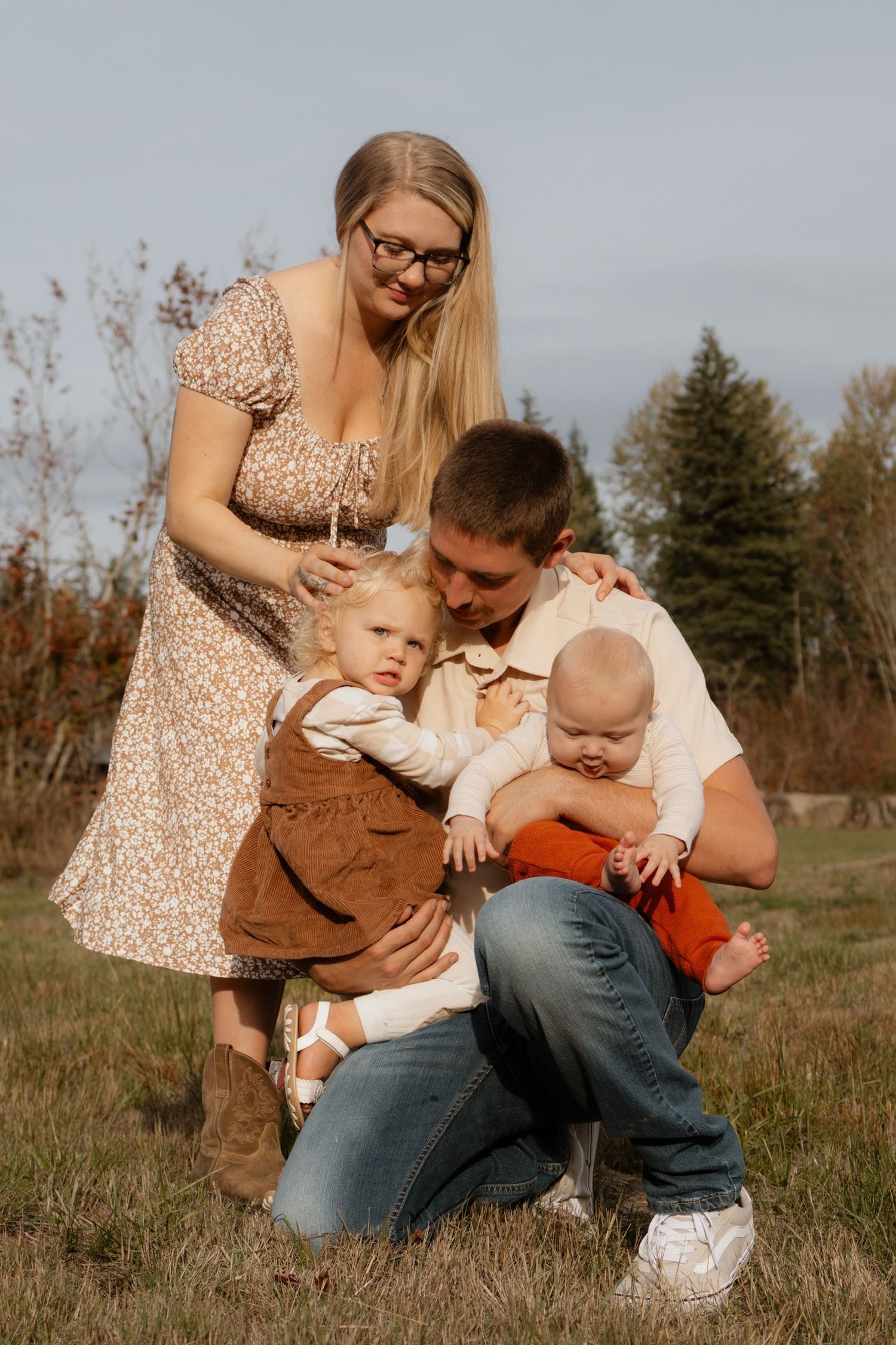 Family enjoying tender moments together outdoors in a grassy field on an autumn day wearing coordinated earth tones.
