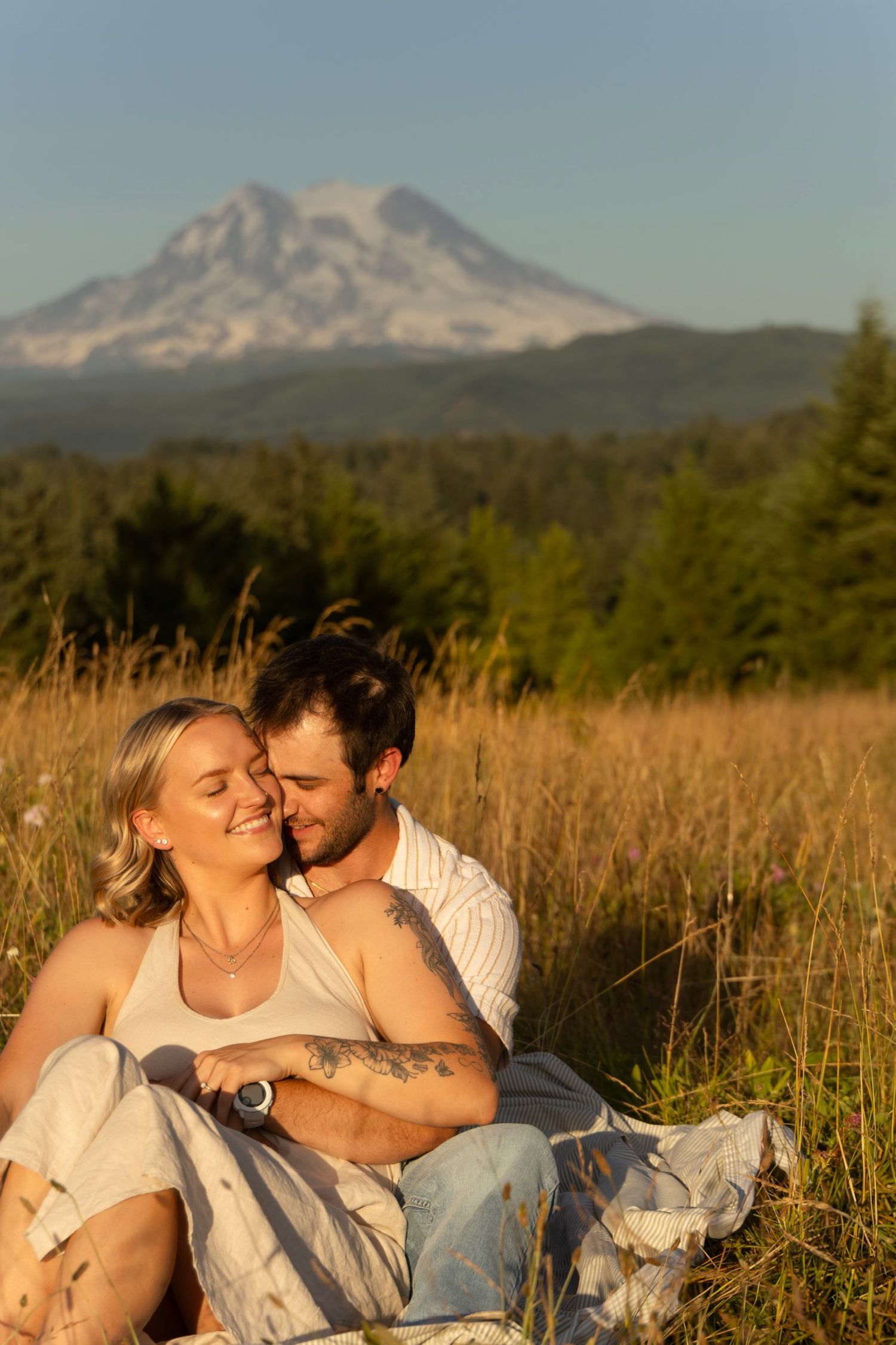 A couple relaxes in a scenic meadow with mountains visible in the background during golden hour.