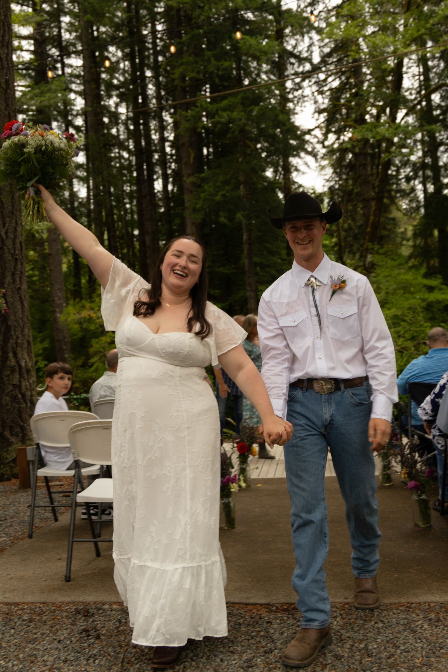A joyful wedding celebration moment on an outdoor deck with tall evergreen trees in the background.