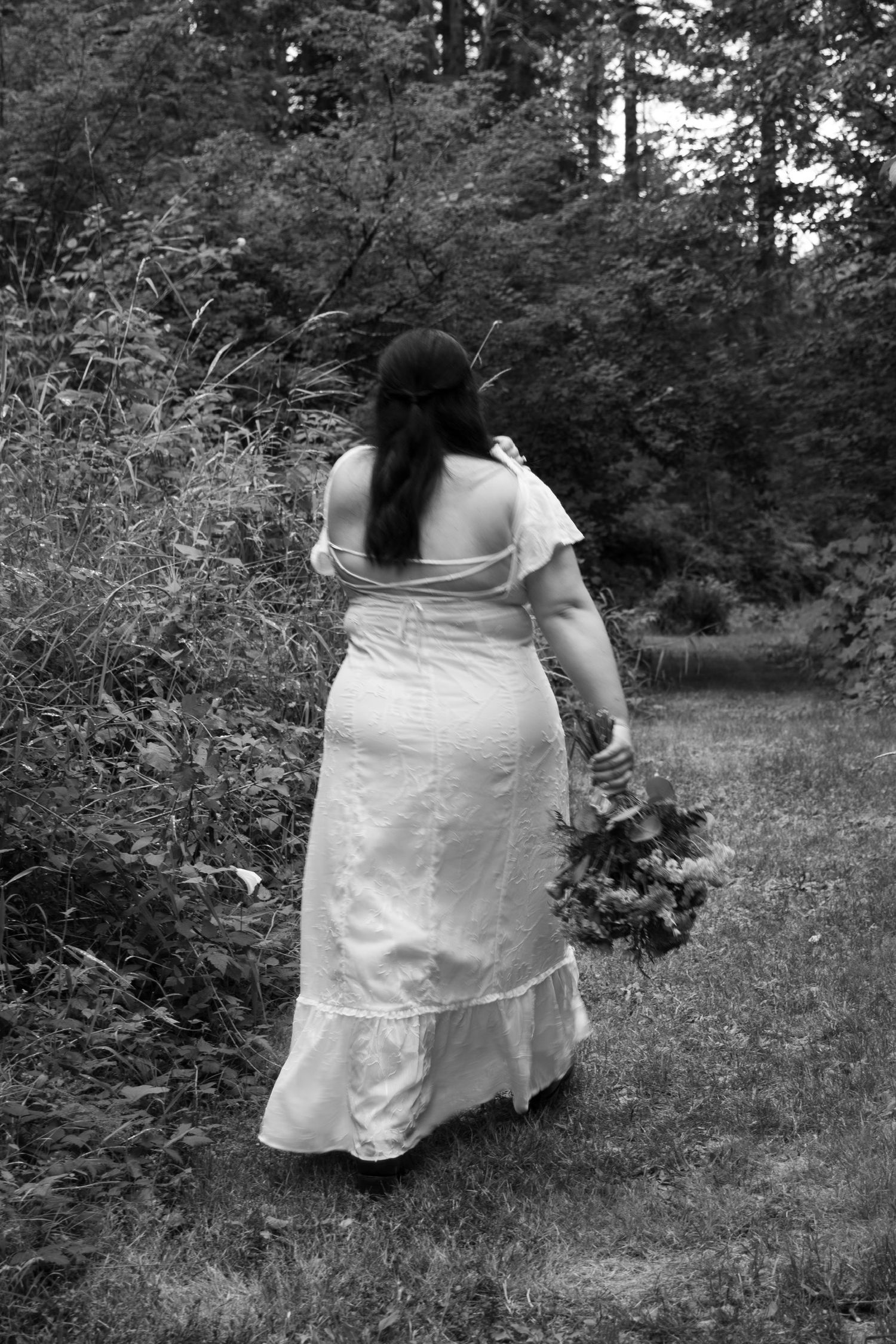 Figure in white dress walking through a wooded area in black and white.